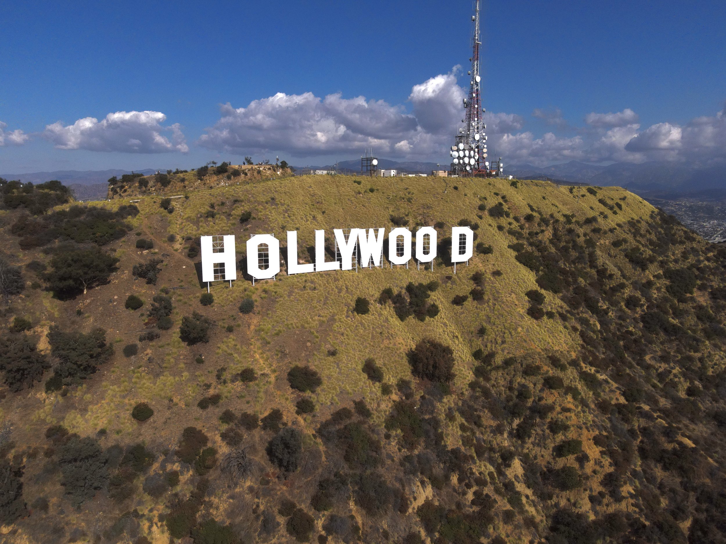 A large Hollywood sign on a hillside, with a radio tower nearby, under a partly cloudy sky.