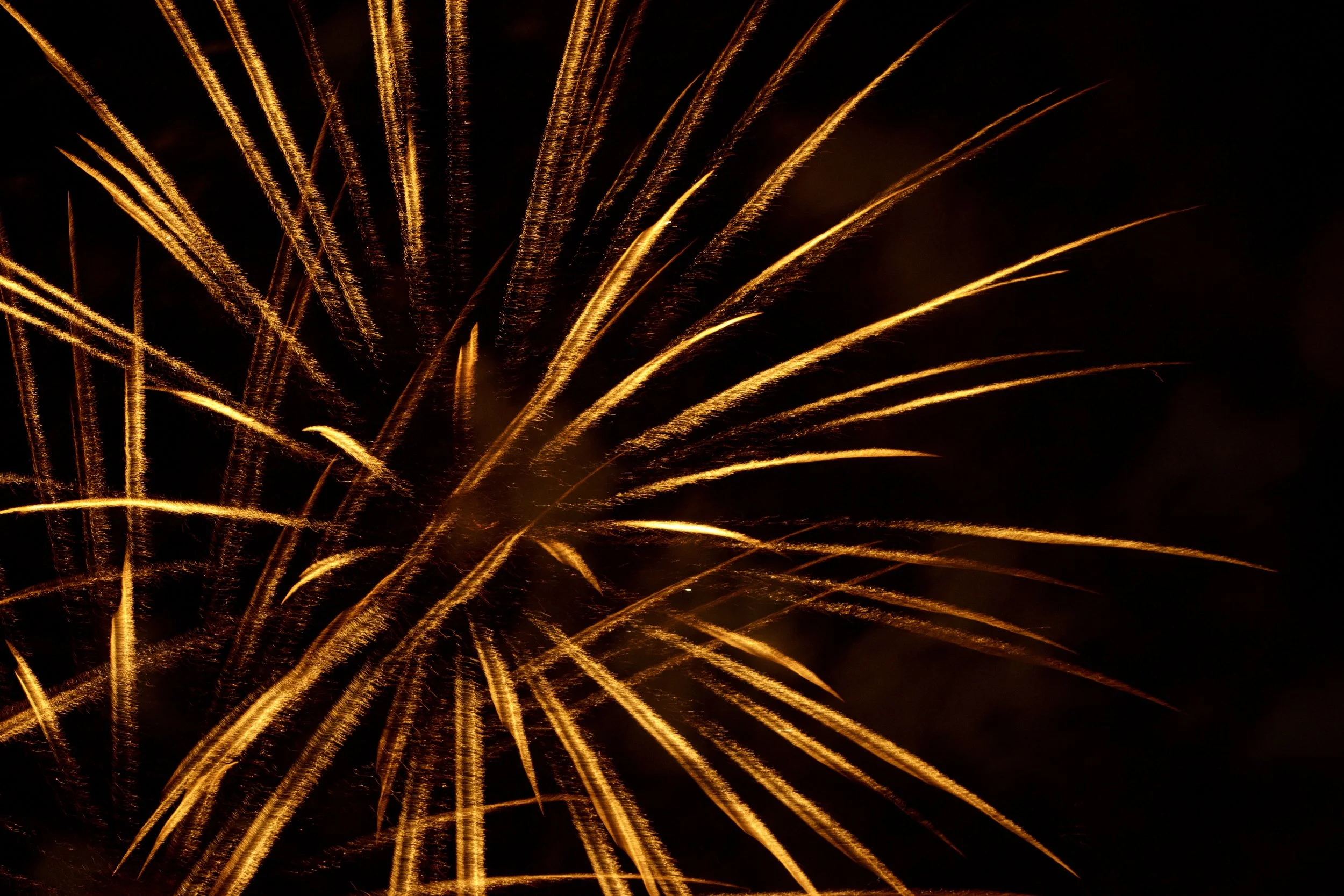 Bright yellow and orange fireworks exploding in the night sky with streaks of light radiating outward.