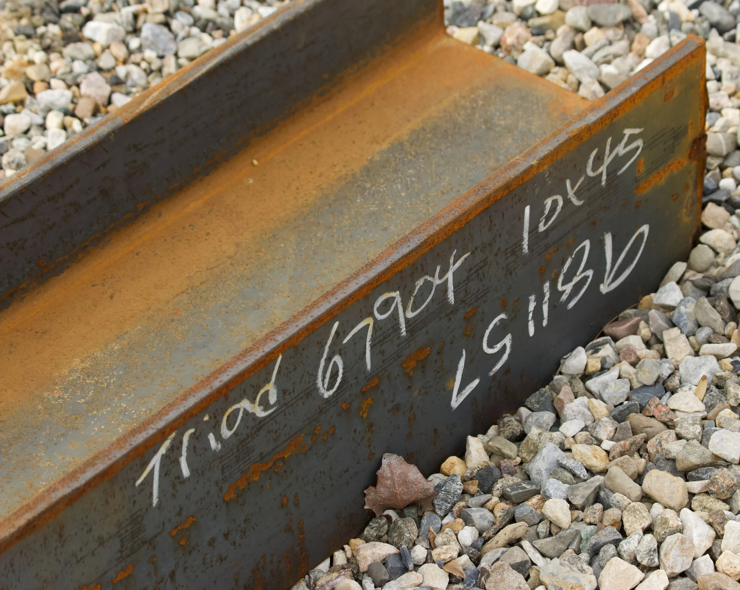 Close-up of a rusty metal gravel board with white chalk writing, surrounded by small gray, white, and beige rocks.