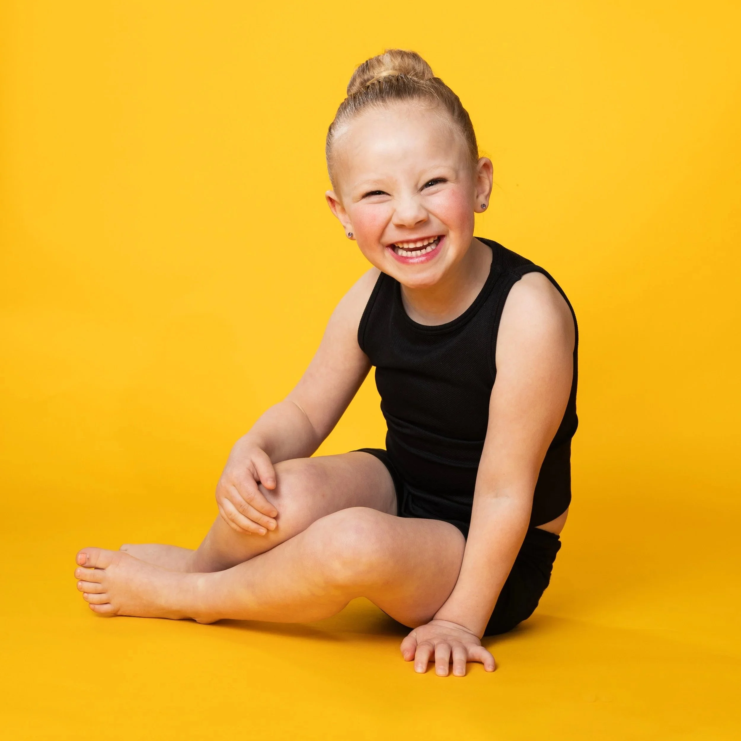 young girl in black dance outfit sitting on the floor smiling at camera