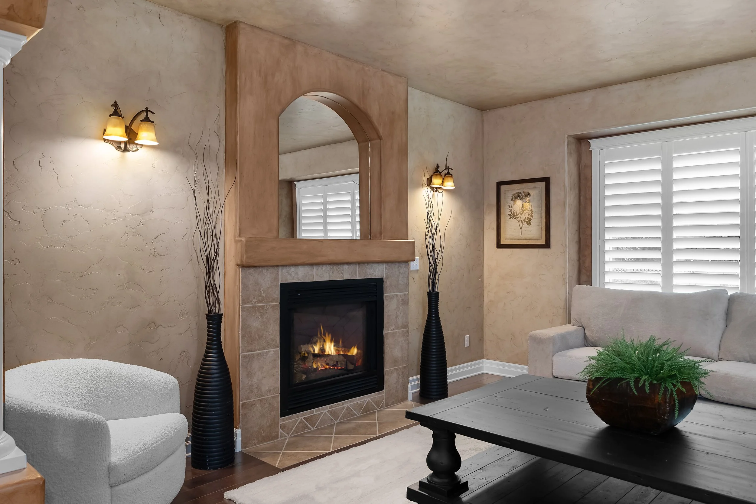A zoomed in detailed shot of a fireplace, and a modern home with stucco walls, white furniture, black vases on either side of the fireplace and a green plant on the table