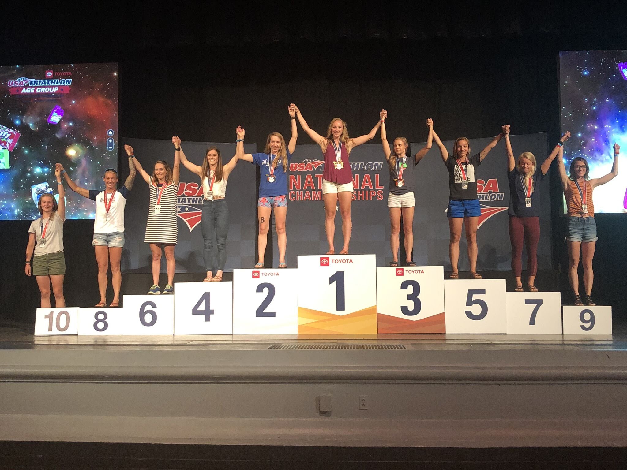 Podium with female athletes celebrating at USA Triathlon National Championships, displaying medals and numbered placements from 1 to 10.