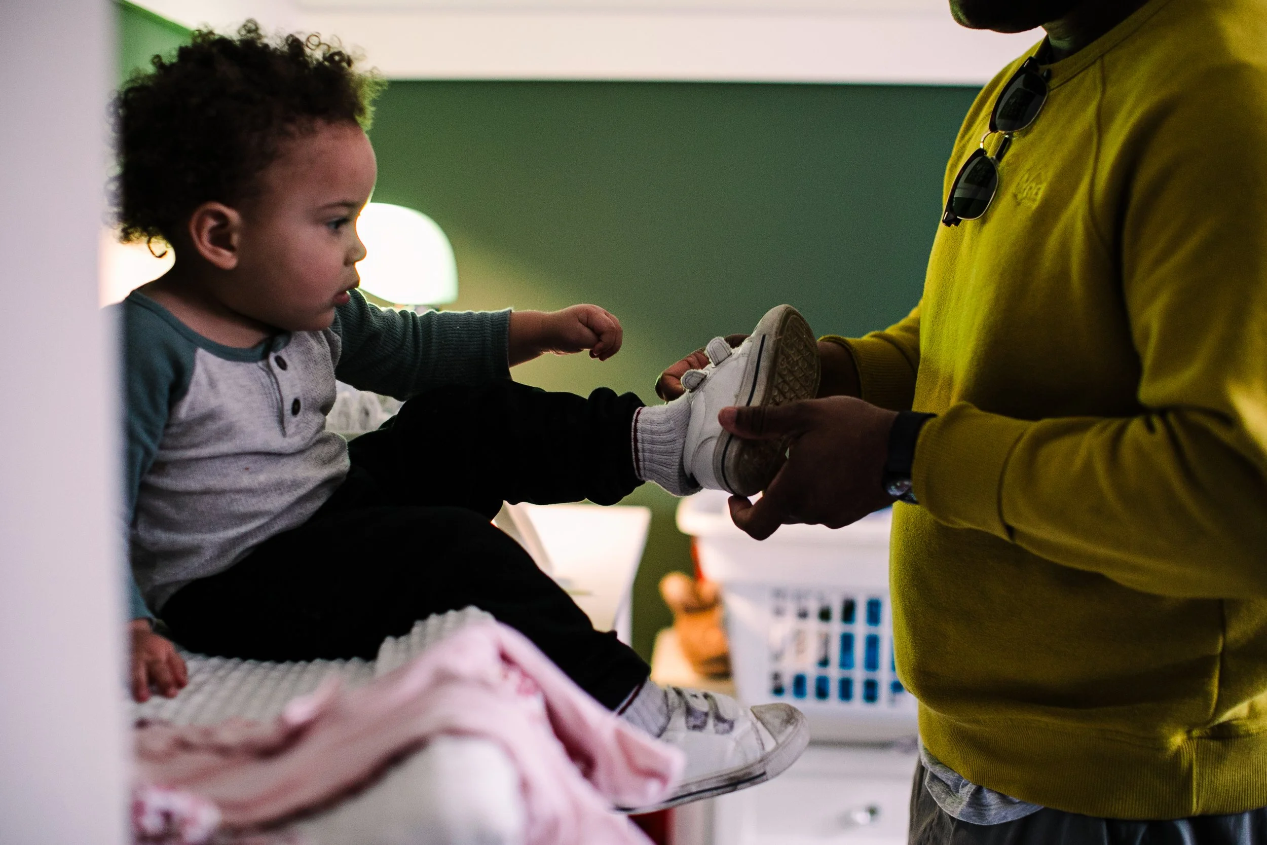 Atlanta Family photographer in College Park Georgia captures a father helping his young son put his shoes on while sitting on the changing table in his bedroom.