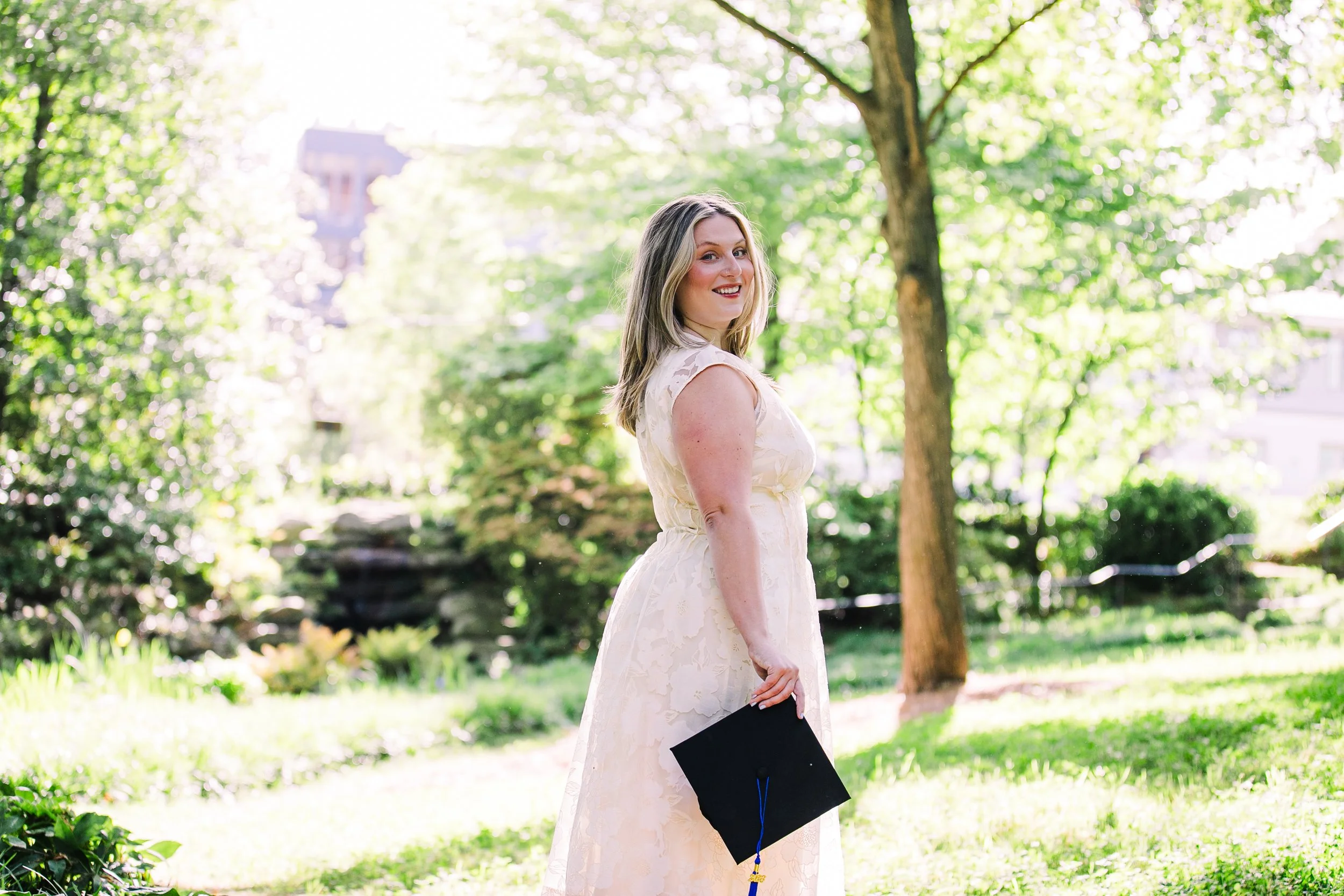 Young graduate student posing with a graduation cap in a sunlit wooded park in Atlanta called Winn Park