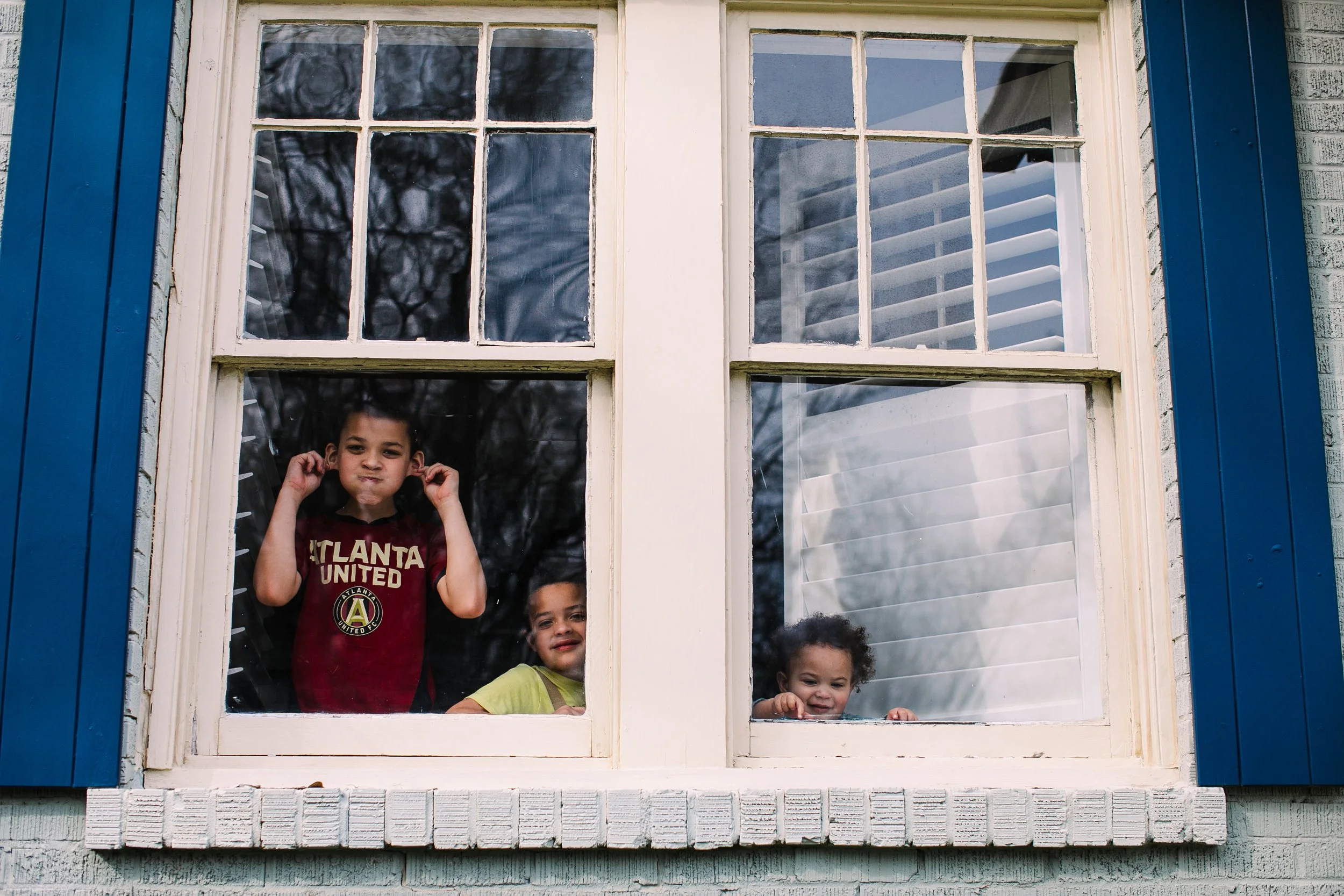 Atlanta Family Photography of three boys looking out through the window of their house making silly faces at the photographer
