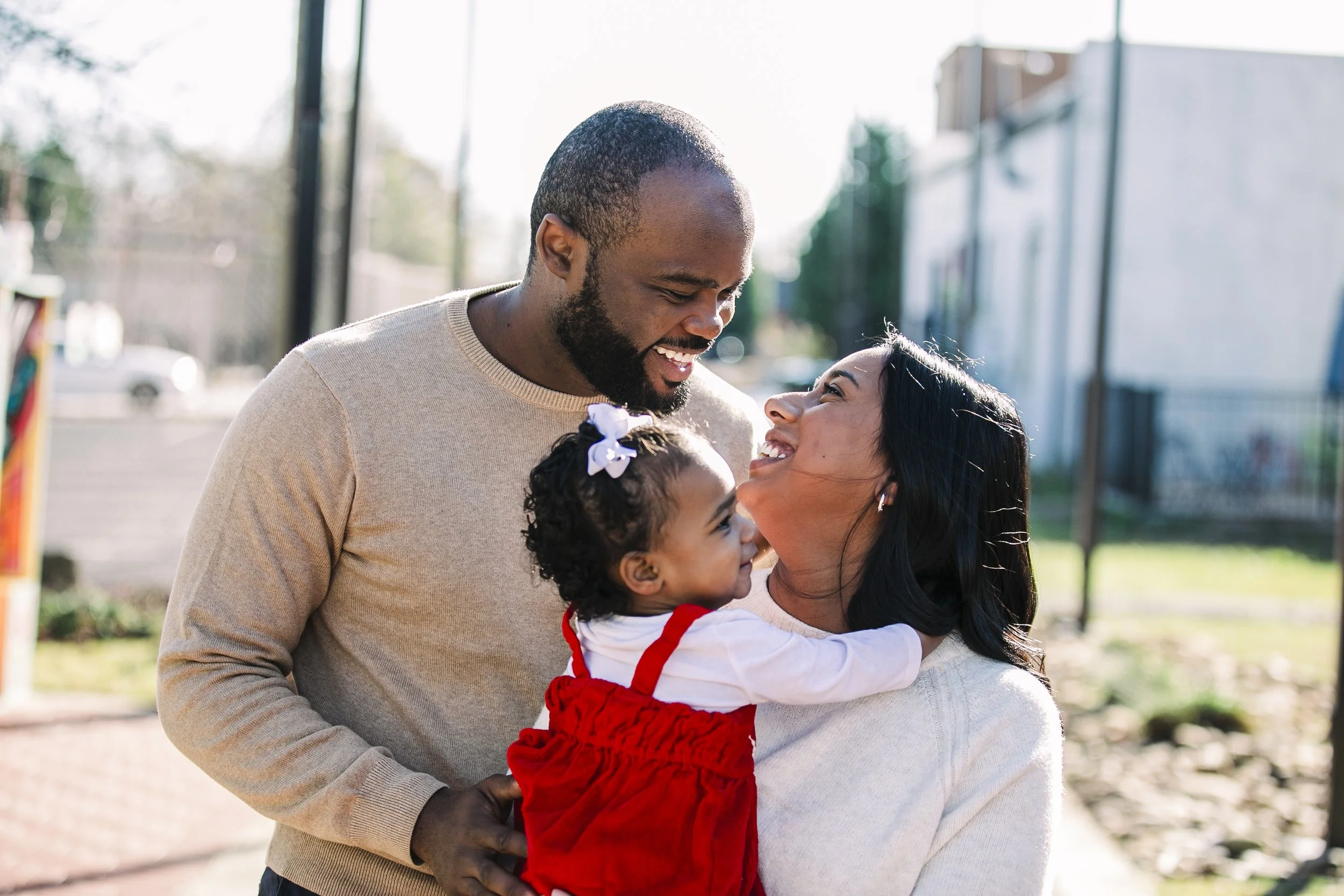 Atlanta Family Photographer captures family photo with father, mother, and little girl in a bright red dress on a sunny day in Hapeville Georgia