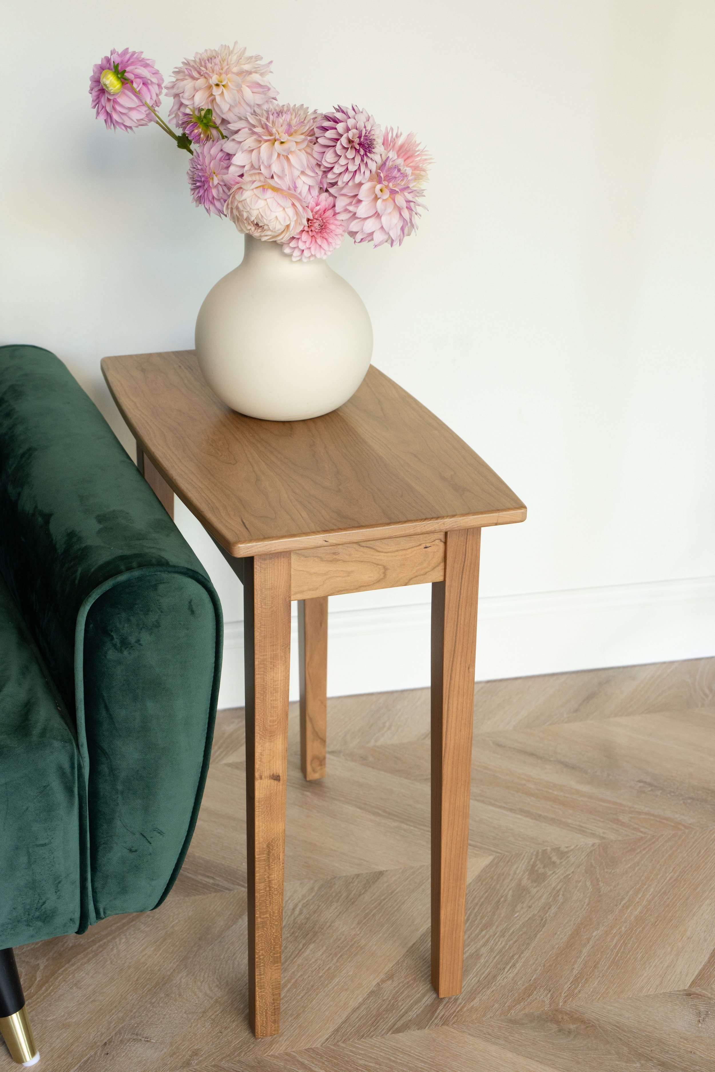 a shaker style end table made from cherry wood with a vase of flowers on top and next to a sofa