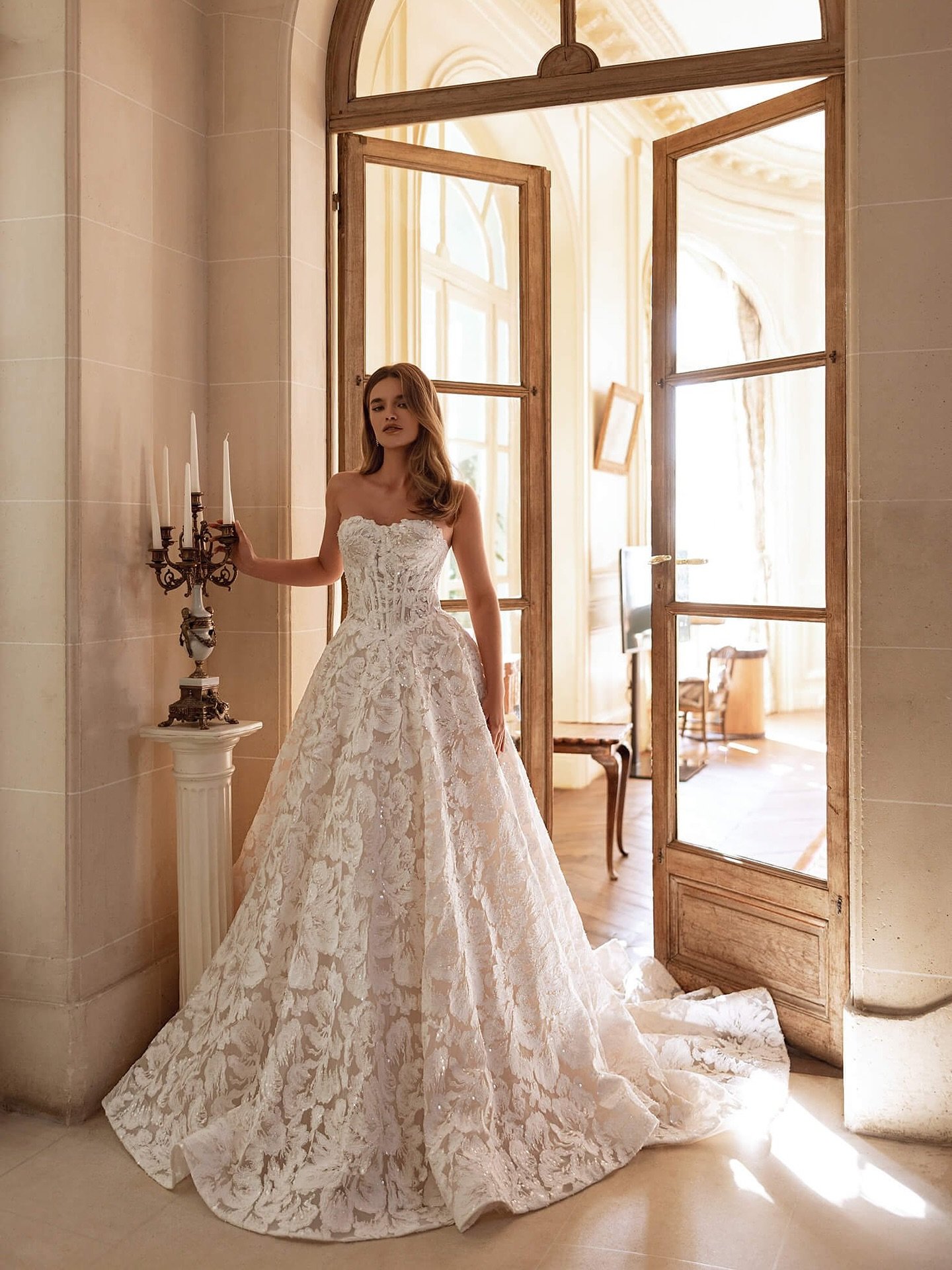 Bold florals, couture craftsmanship, and just the right touch of sparkle ✨ The Lala gown stuns with allover lace, a sculpted strapless bodice, and a dramatic train that brings the romance. Ready to turn heads? 💐 #BridalStyle #LaceWeddingGown #Modern