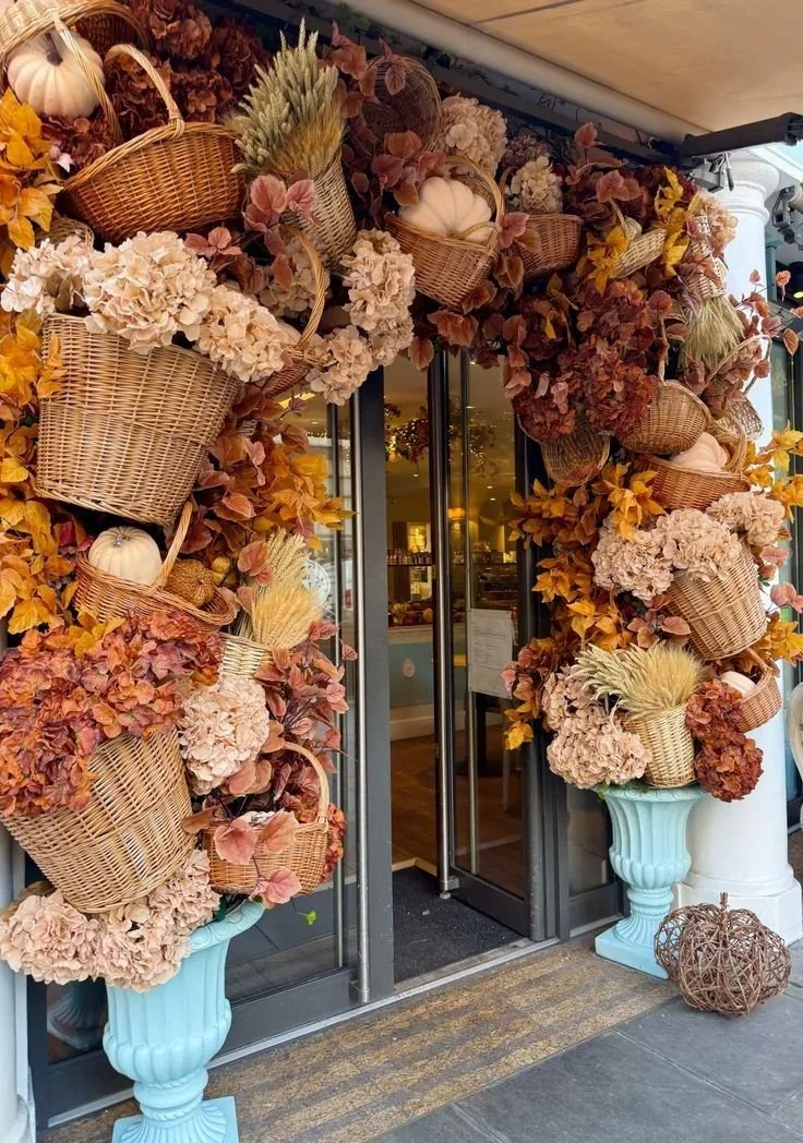 Fall storefront entrance framed with woven baskets, hydrangeas, foliage and pale pumpkins
