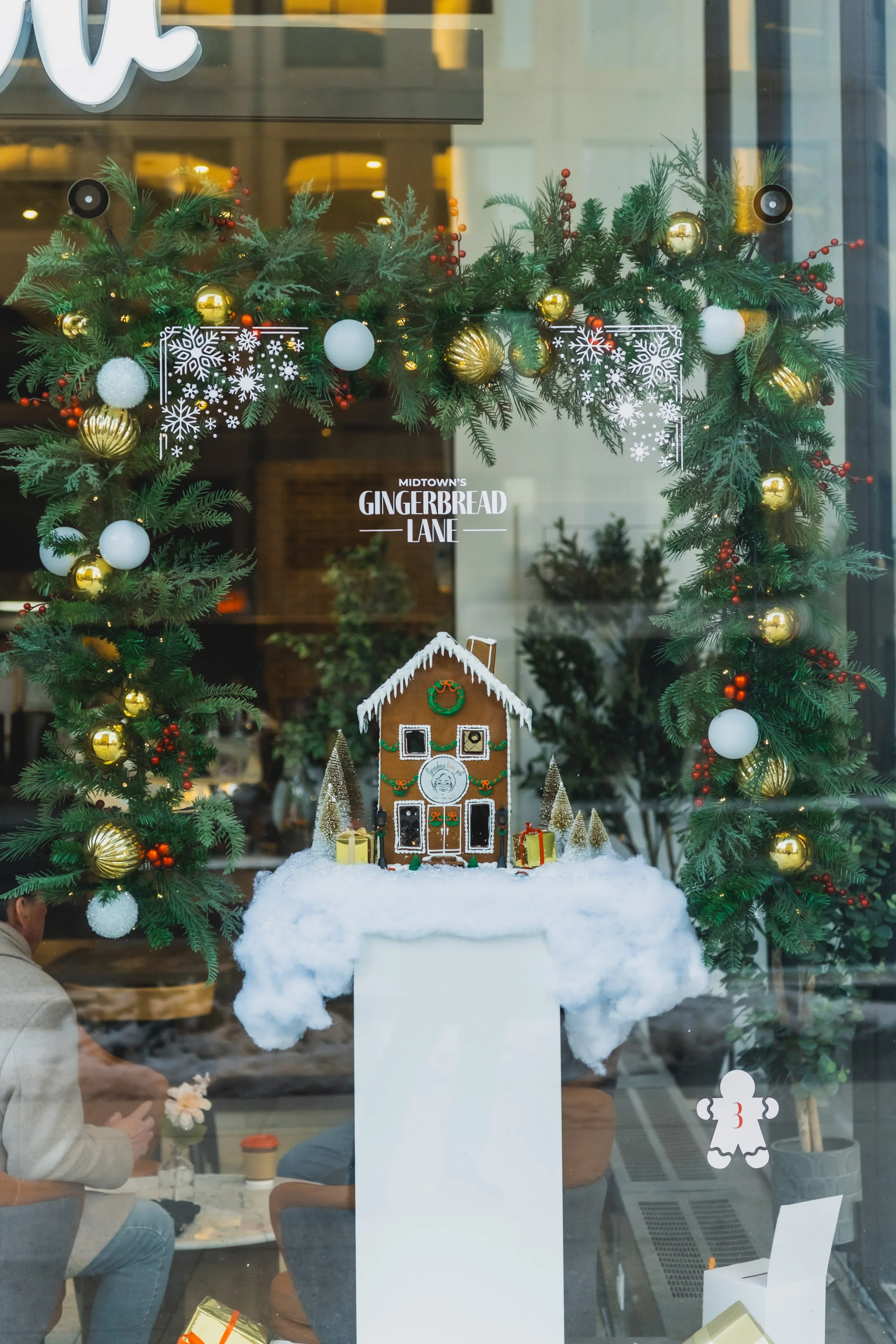 Holiday window installation with a central gingerbread house framed by garland and snow textures for Midtown’s Gingerbread Lane at Yonge St. Clair BIA.