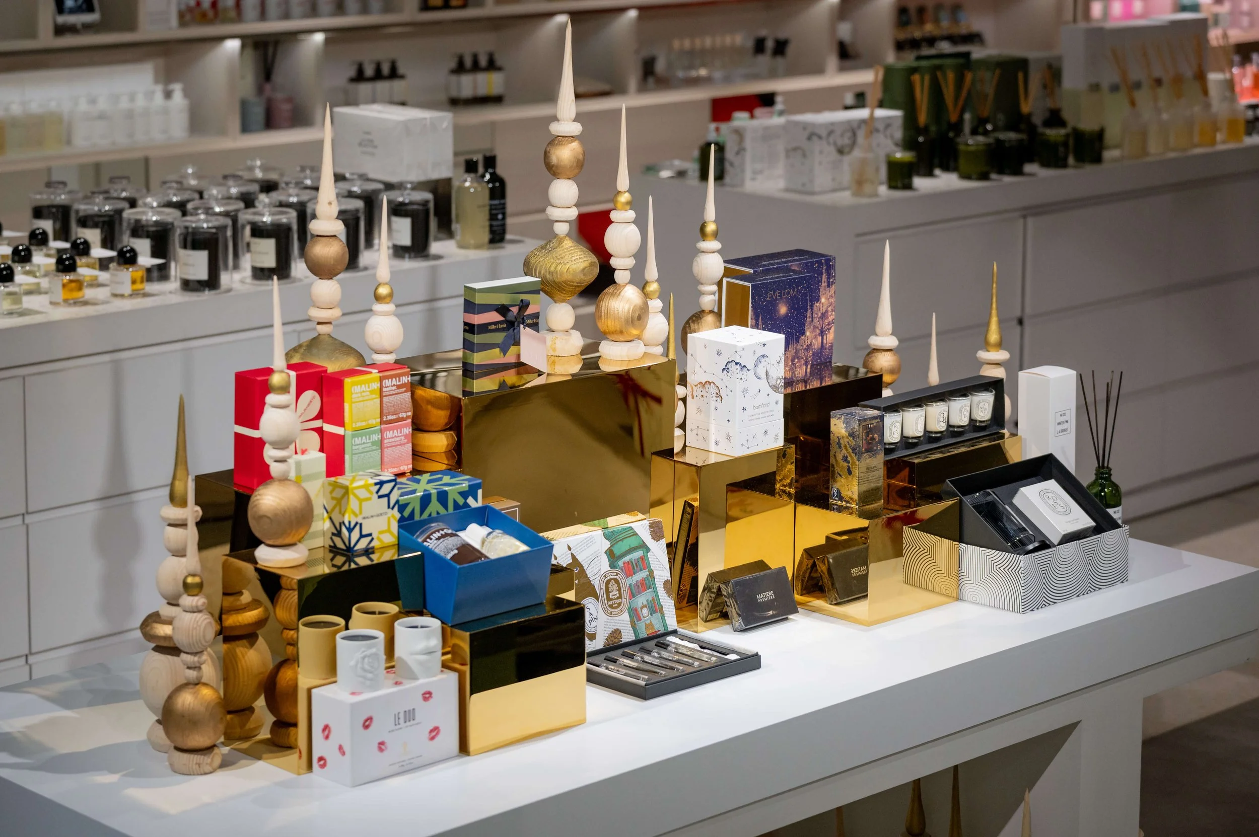 Elevated holiday gift table featuring fragrance, skincare, home scent and boxed gift sets arranged with varied heights and metallic accents.