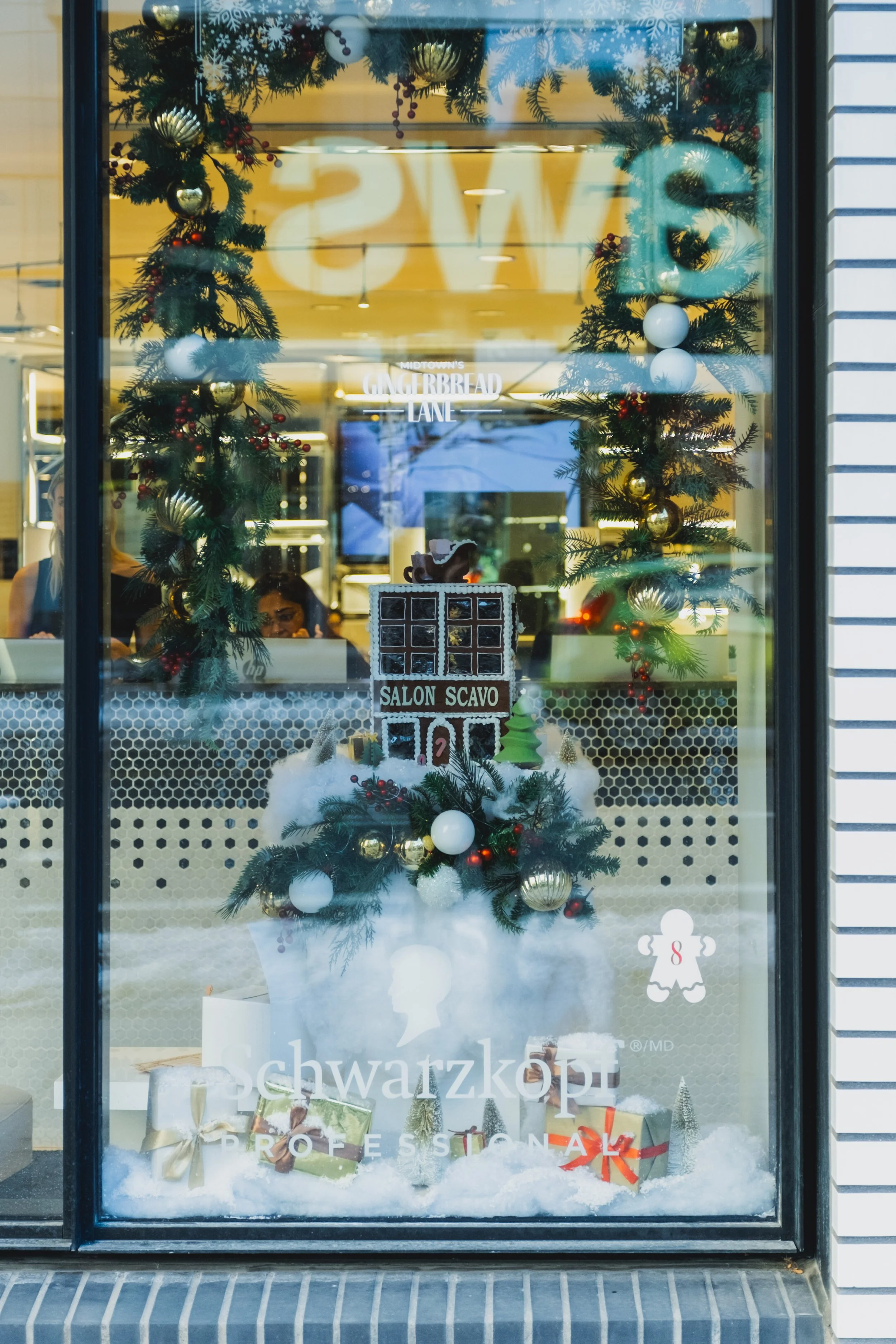 Festive storefront window display for Midtown’s Gingerbread Lane featuring a gingerbread shop scene, snow props, and layered holiday merchandising at Yonge St. Clair BIA.