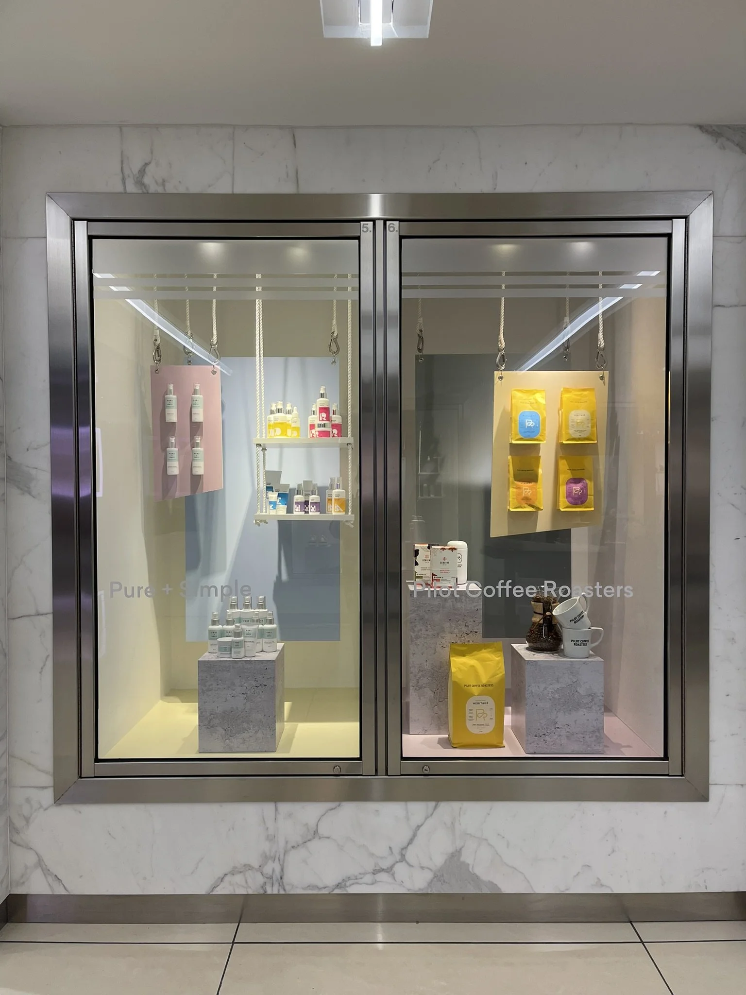 Dual tenant window displays at Manulife Centre featuring Pure + Simple and Pilot Coffee Roasters, unified through coordinated visual merchandising within a shopping centre showcase.