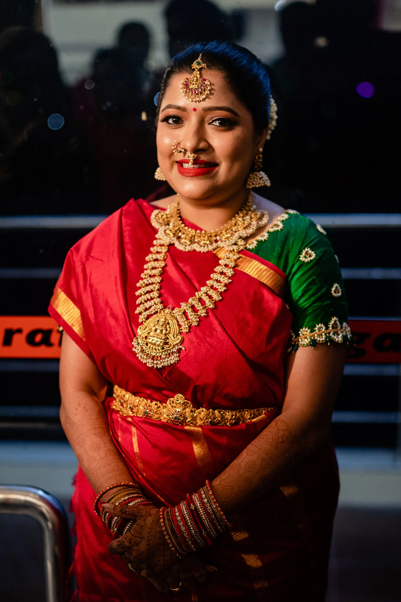 Woman dressed in traditional Indian attire with gold jewelry, red and green sari, and henna on her hands.