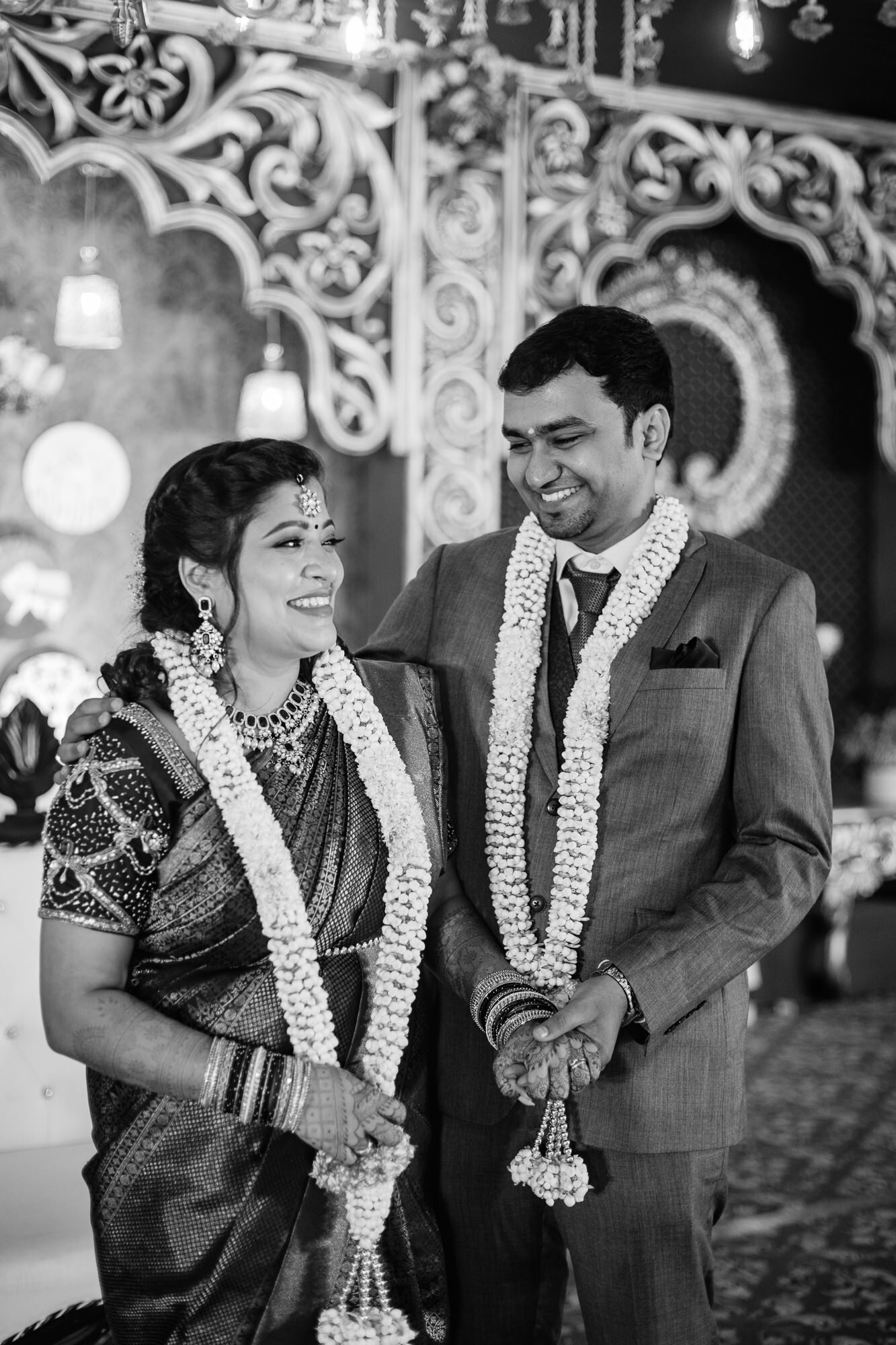 A newlywed Indian couple smiling, wearing traditional garlands and jewelry, during their wedding ceremony.