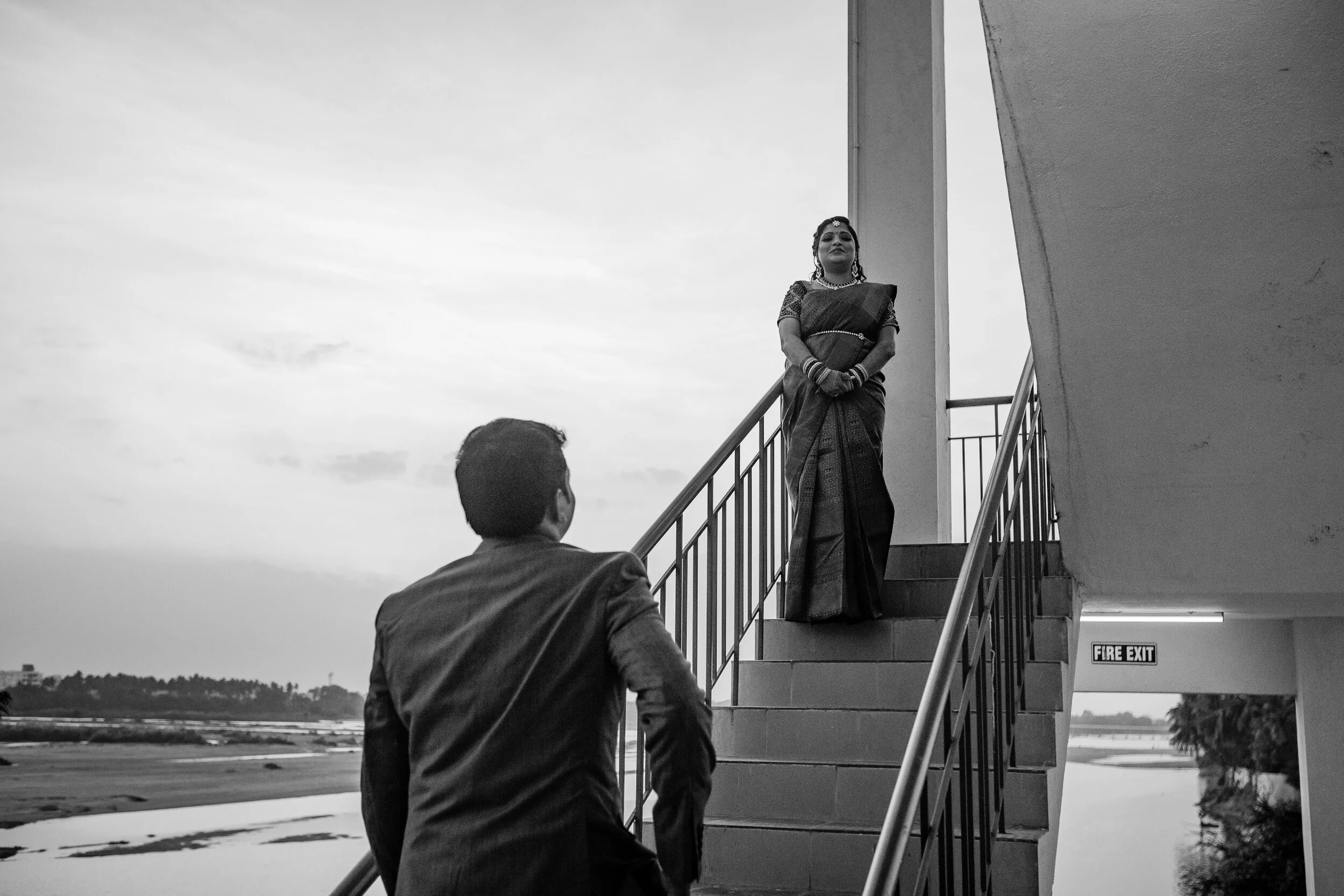 A man in a suit looking at a woman dressed in traditional attire standing on a staircase.