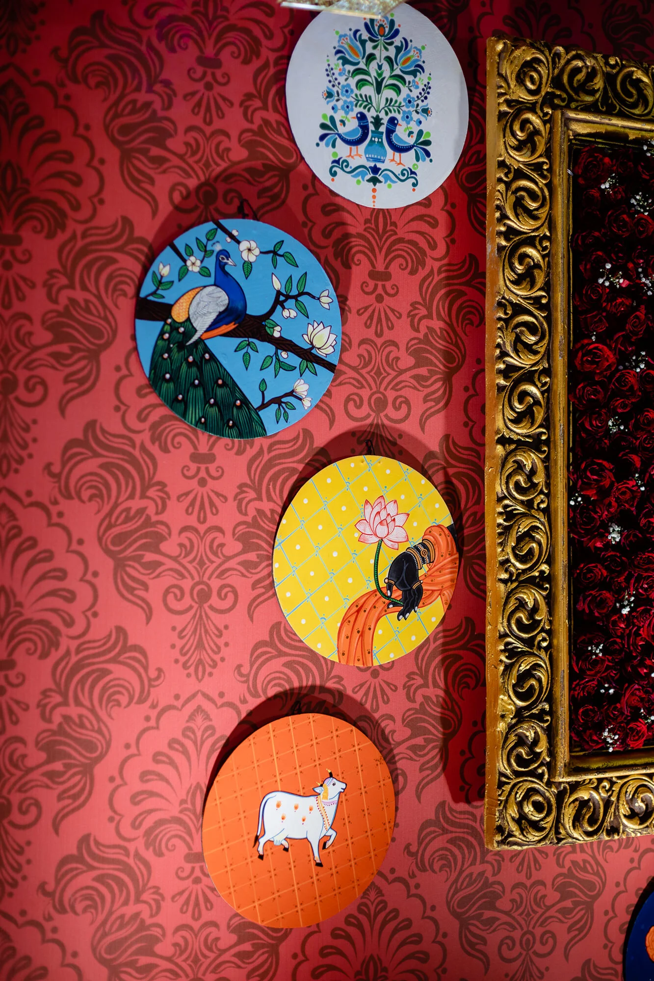 Decorative wall featuring four round illustrations with designs of animals and plants, including a peacock, a cow, and floral motifs, framed by ornate gold detailing.