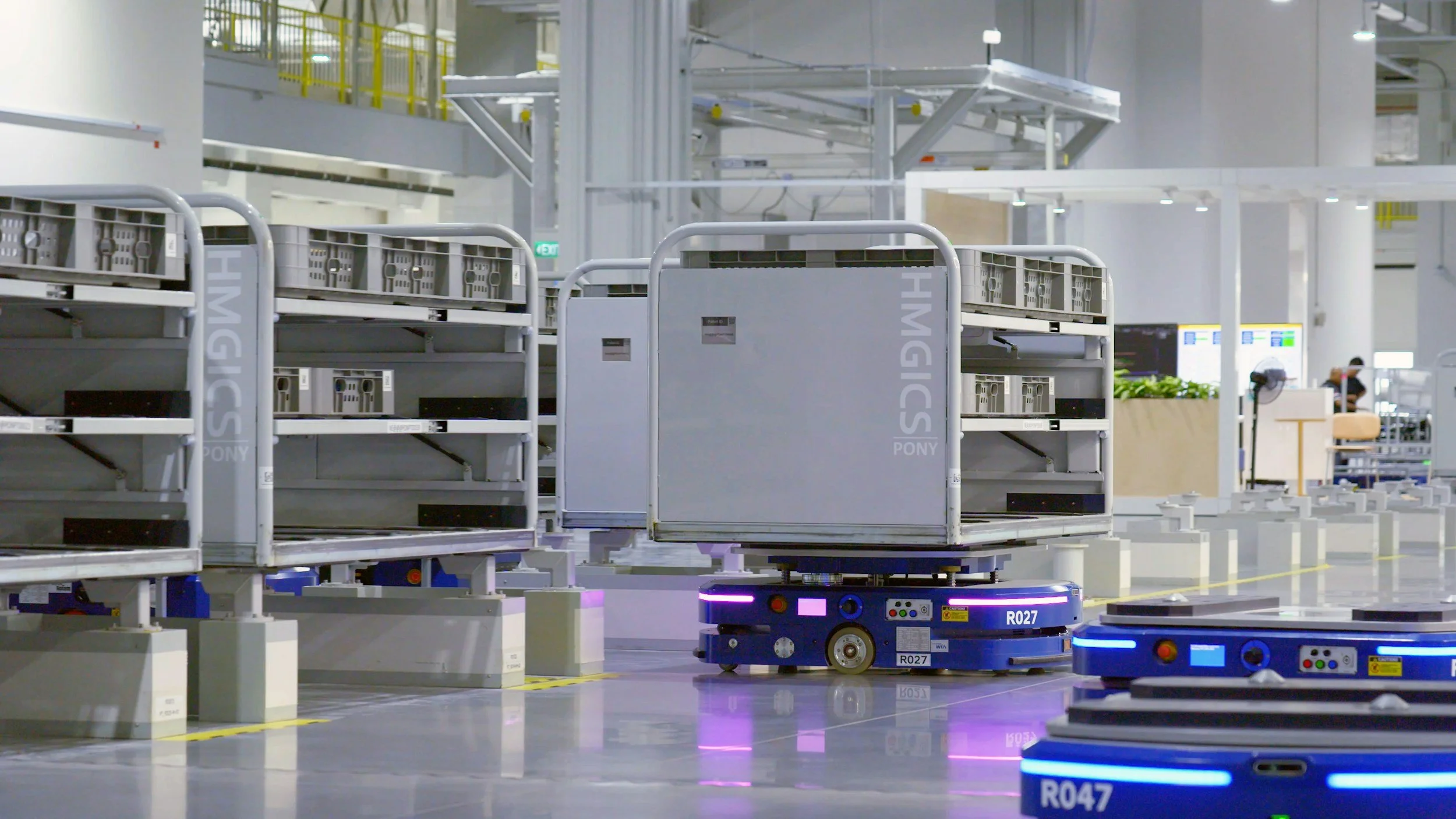Autonomous robots transporting luggage or equipment inside a modern, spacious facility with white and yellow structural elements.