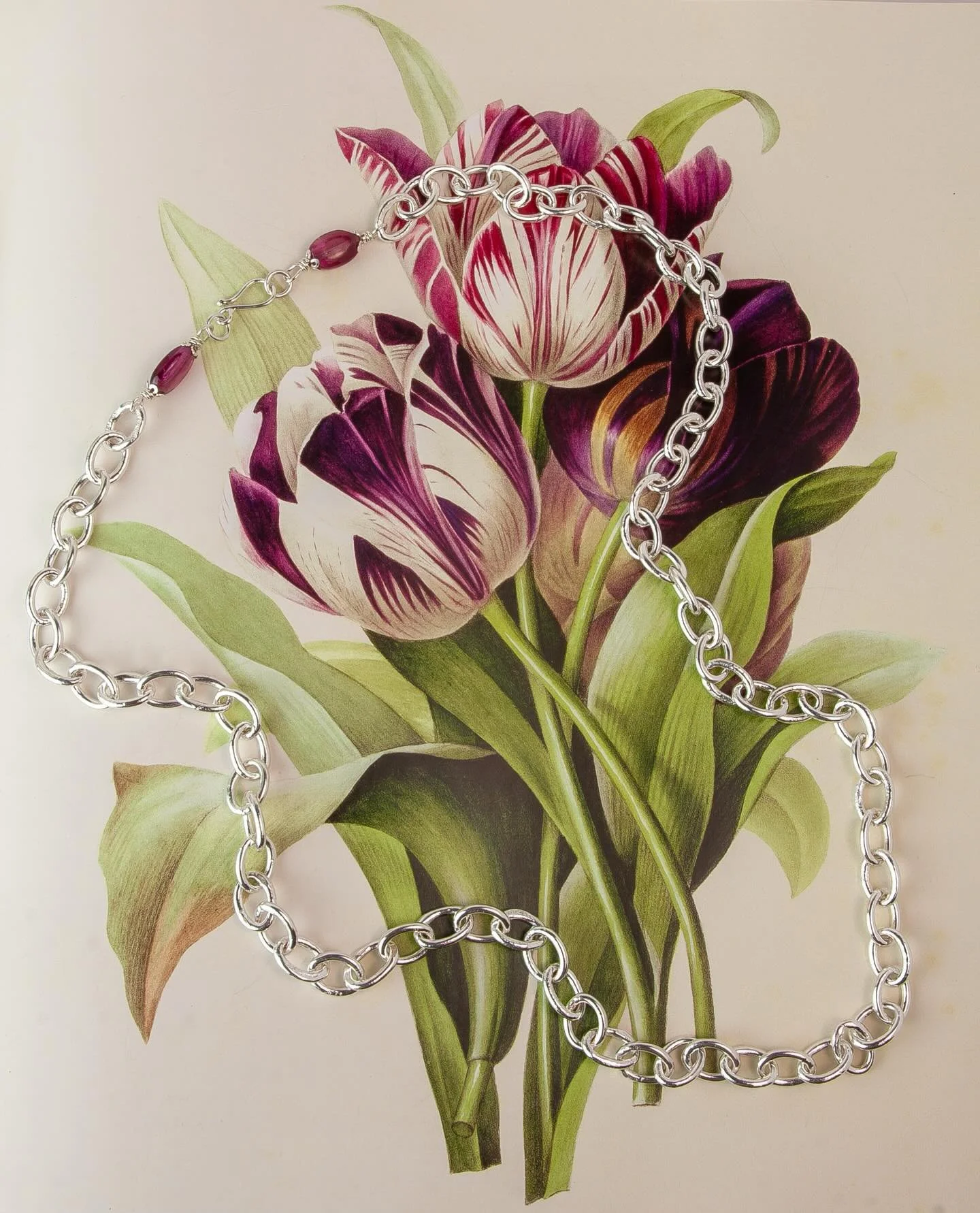 Woven Garden
A heavy, handmade fine silver chain necklace, over 30 inches in length, with bright pink tourmaline beads woven into the clasp. Styled on a book with a vivid floral ground. 

📸 @seanythomas