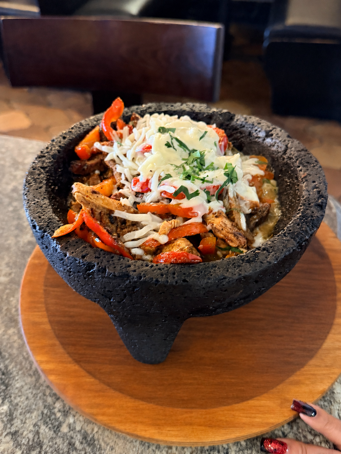 Don Jockey molcajete served in a black stone bowl with grilled meats, vegetables, cheese, and cilantro.