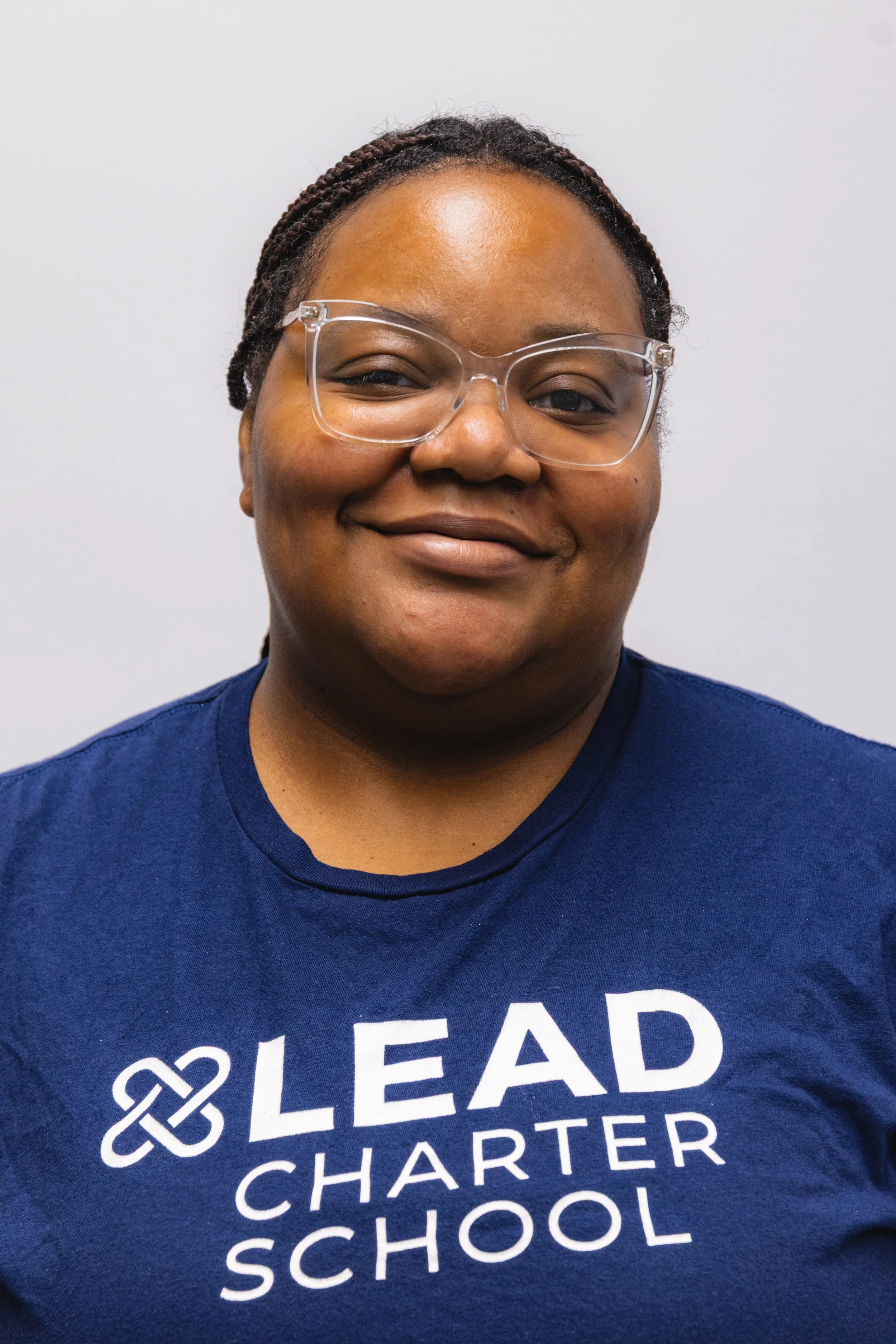 Close-up of a woman smiling, wearing glasses and a blue shirt with white text that says 'LEAD' and other words partially visible.