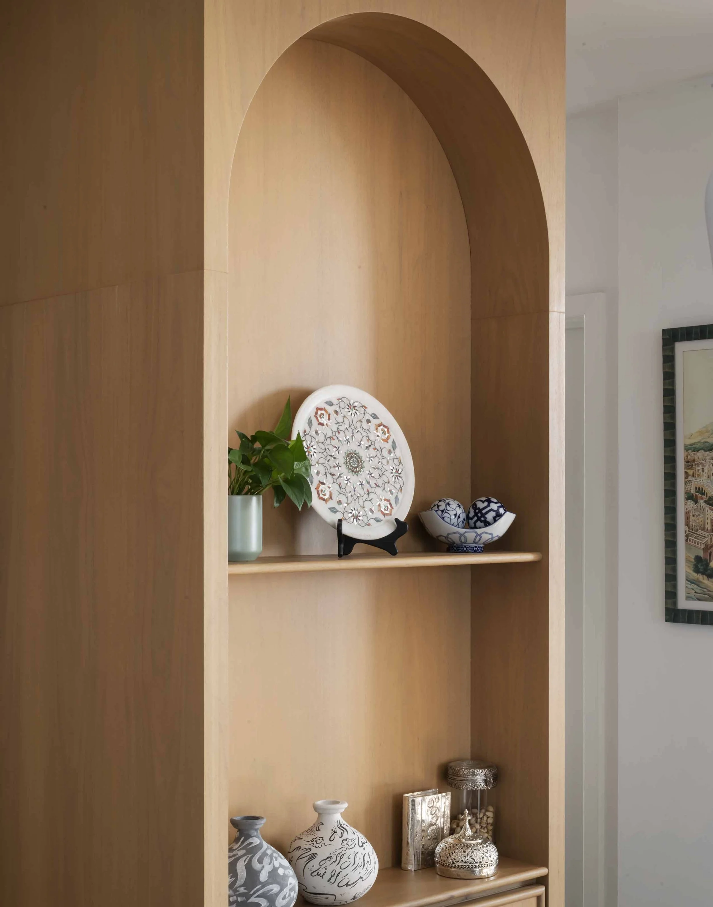 Decorative wooden wall shelf with vases, plates, and small ornaments, including a green plant, displayed in a cozy interior setting.