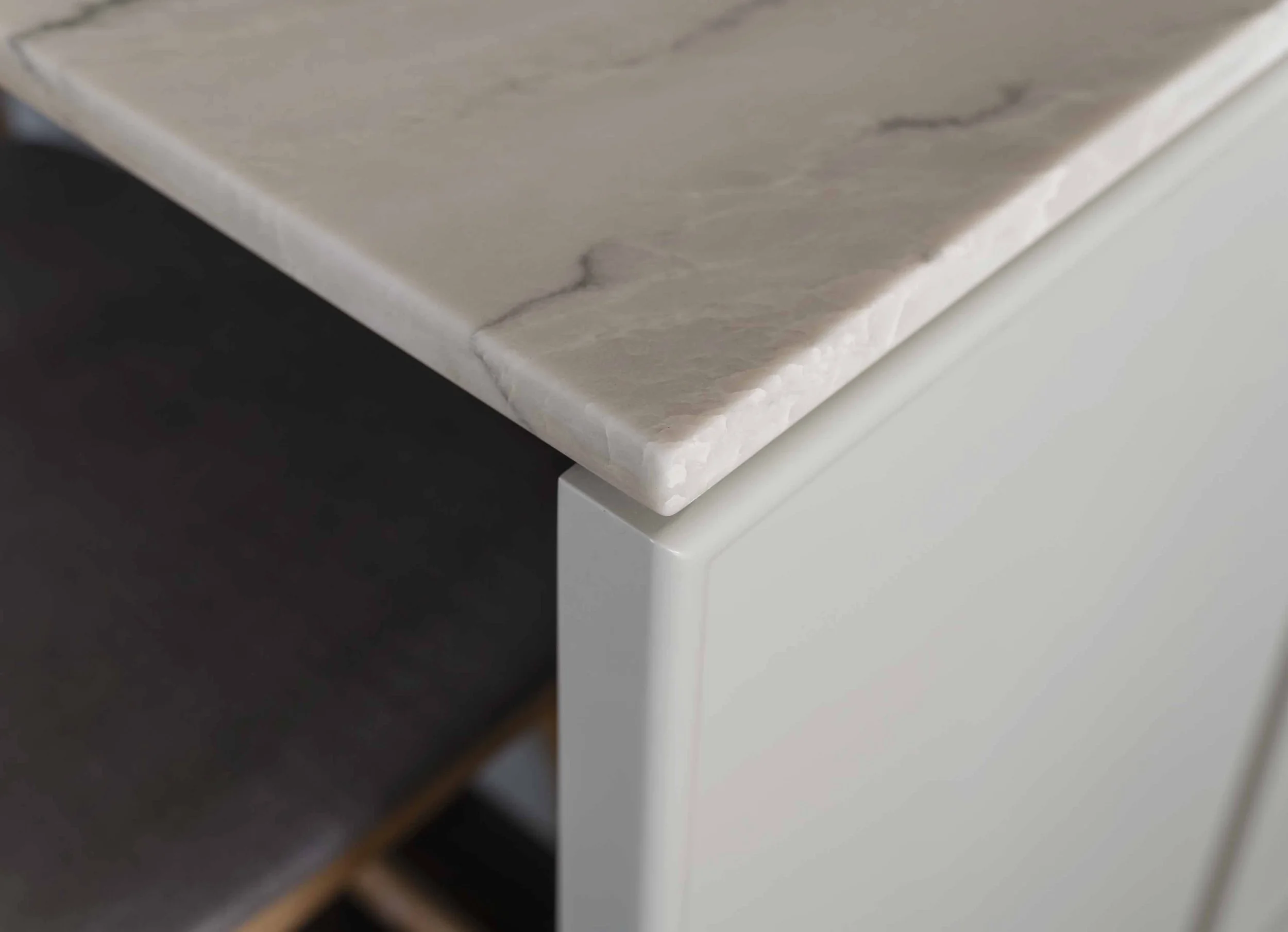 Close-up photo of a marble countertop edge with subtle grey veining, mounted on a white base.