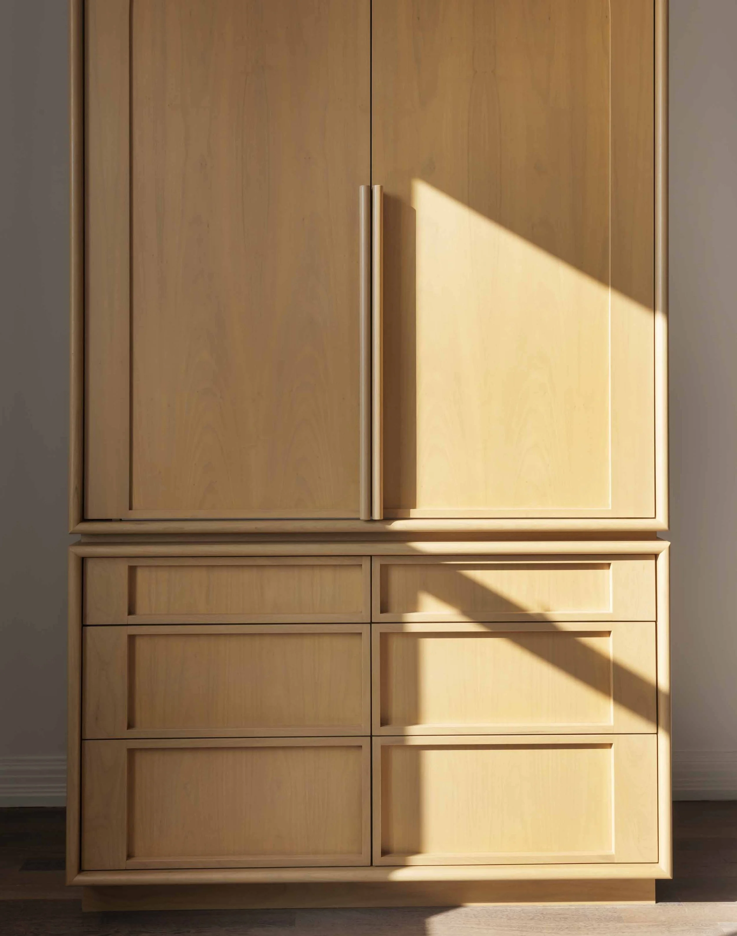 A wooden cabinet with two large doors and multiple drawers at the bottom, featuring vertical handles on the doors.