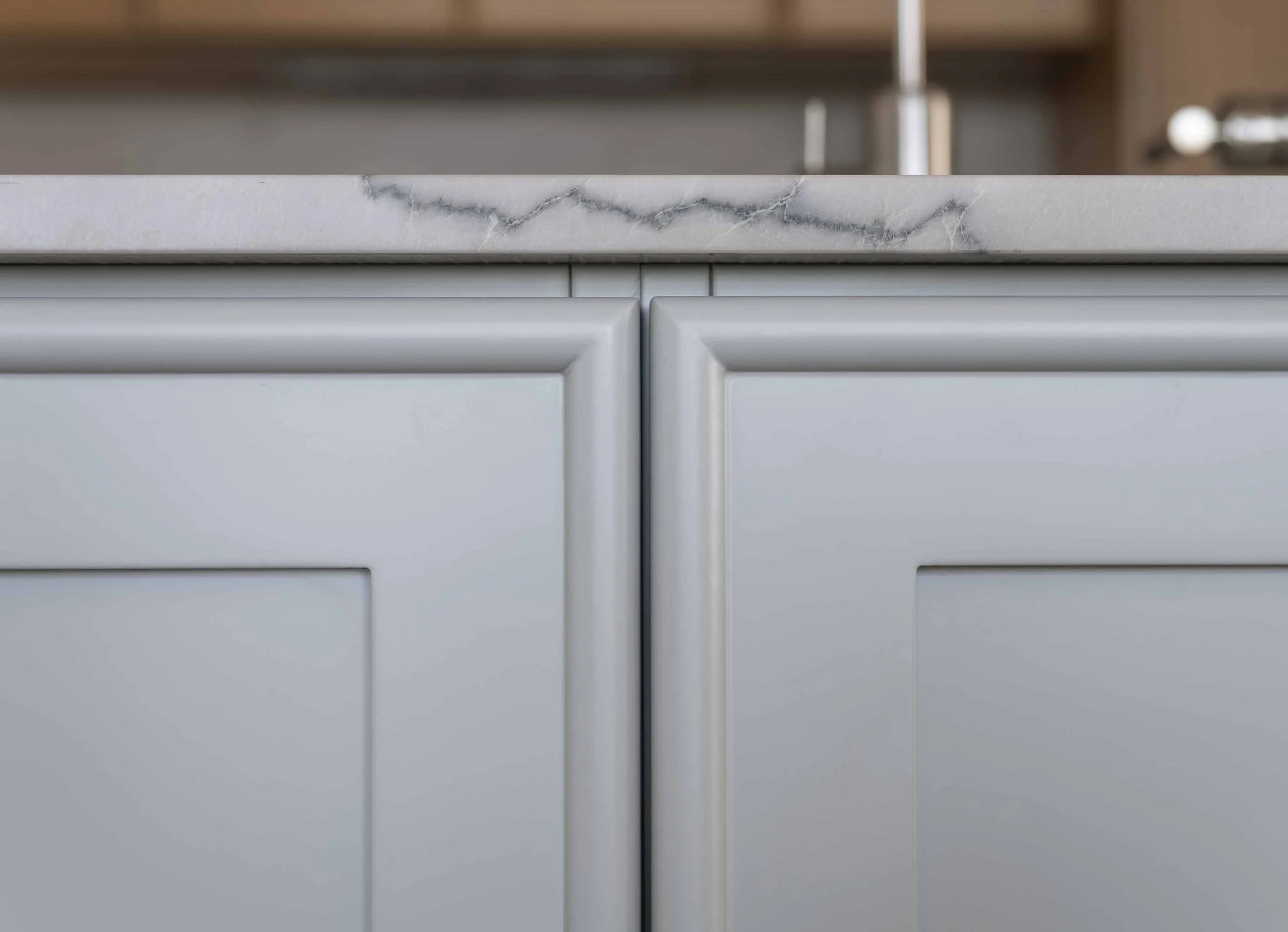 Close-up of a kitchen cabinet or drawer with a white marble countertop showing gray veining, and white cabinetry with a strip of molding.