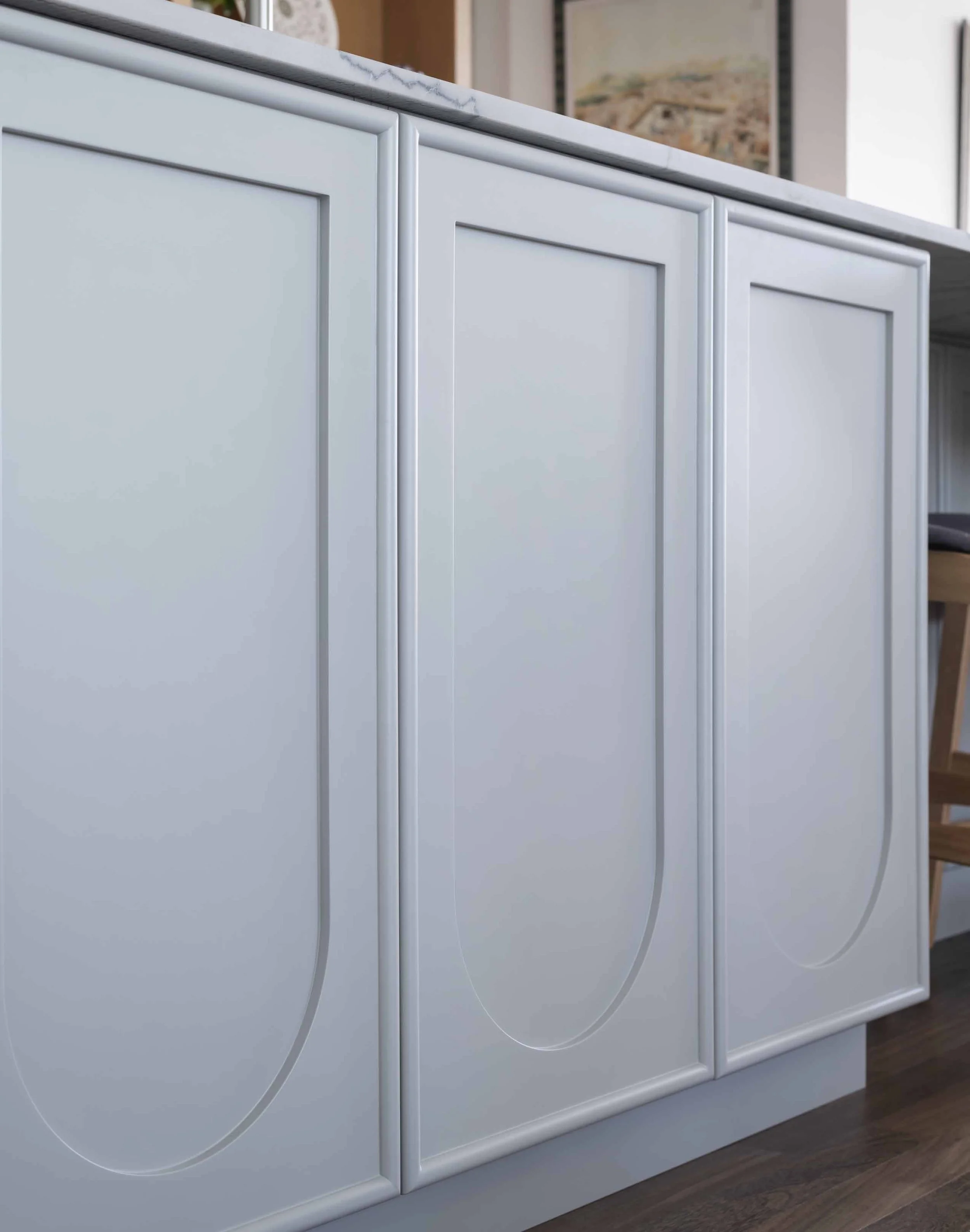 Close-up of white cabinetry with decorative paneling and a marble countertop, next to a partial view of a piece of artwork on the wall.