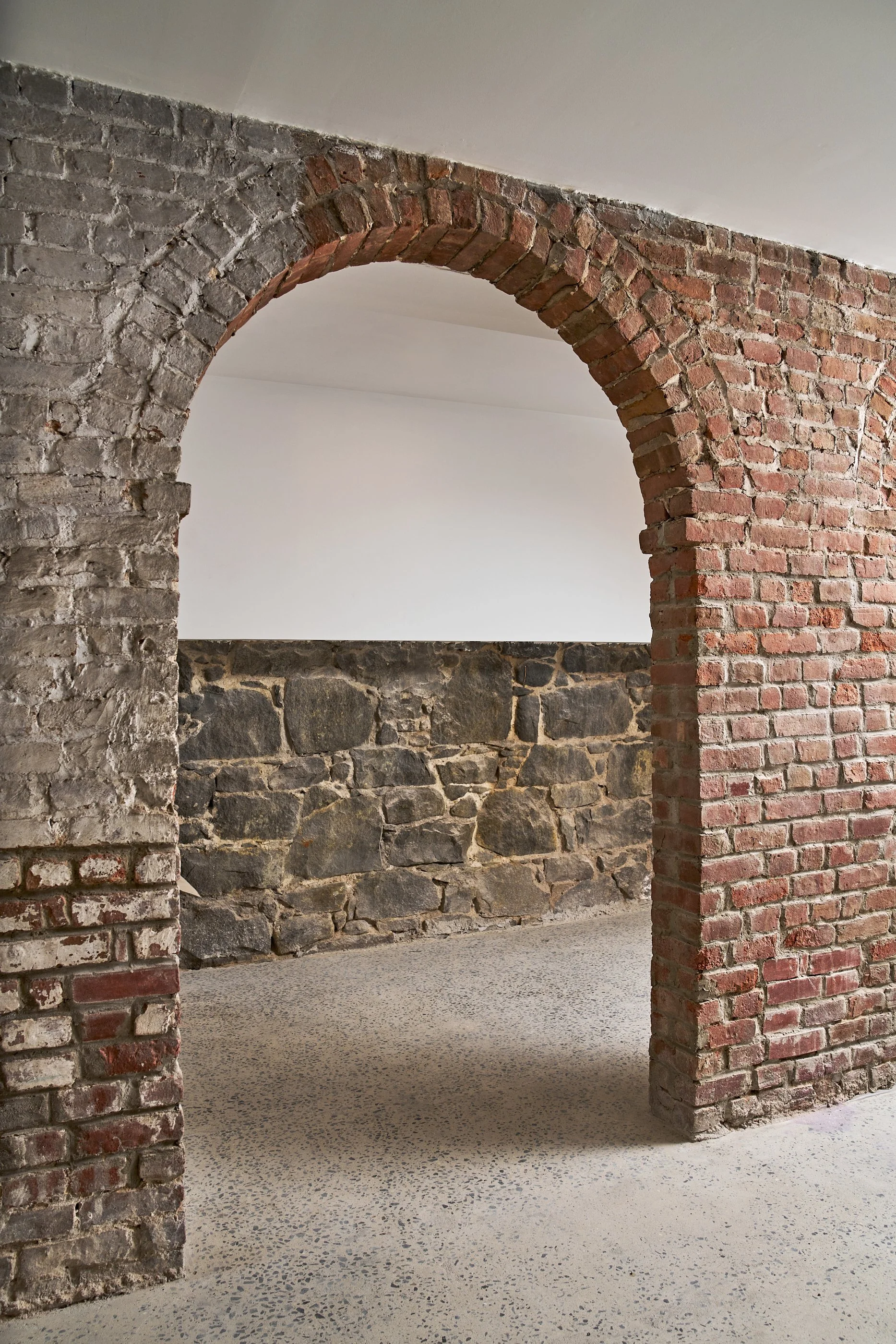 Interior view of a room with a red brick archway, stone wall, and polished concrete floor.