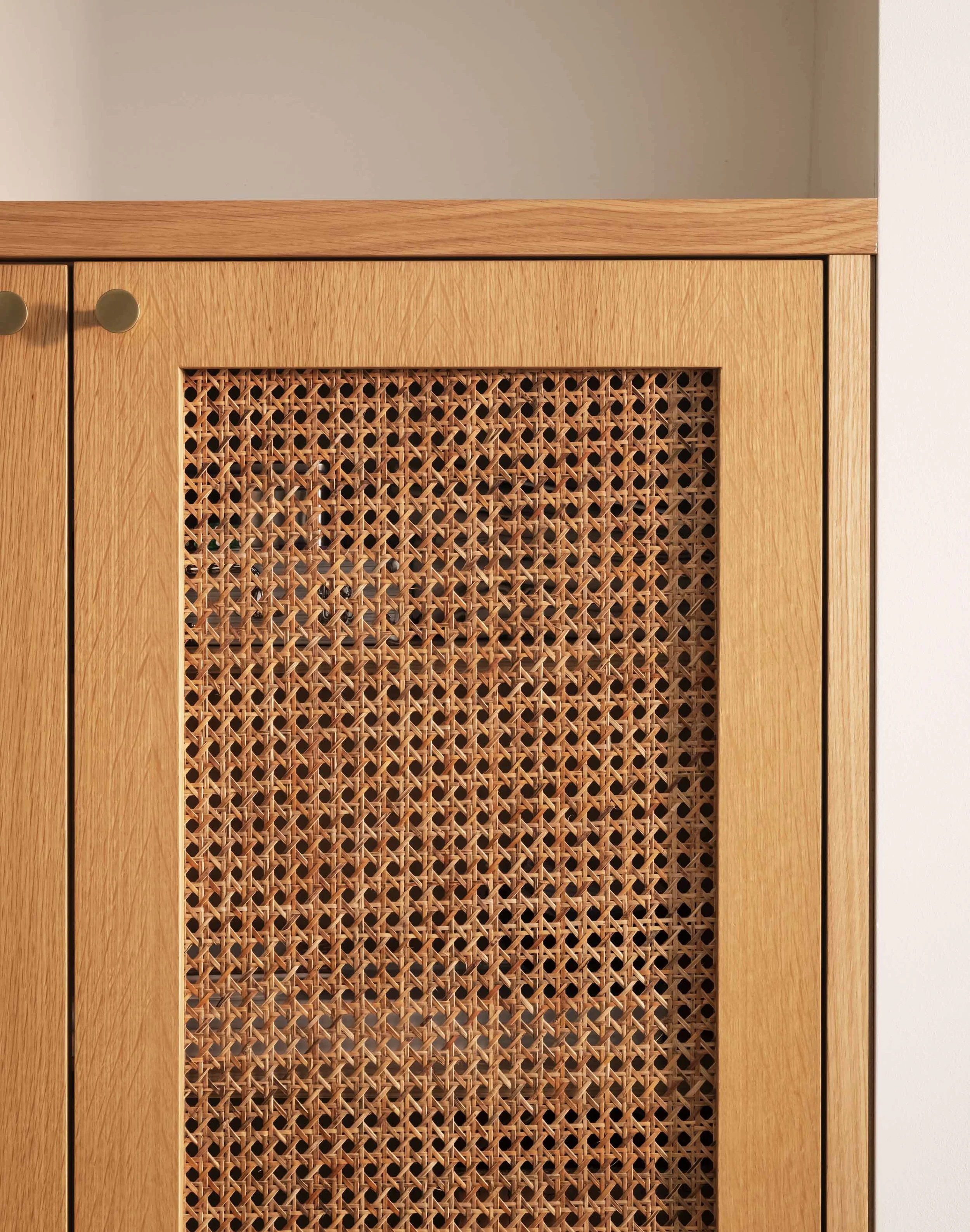 Close-up of a wooden cabinet with a woven rattan panel on the door, round knob handles, and a glass top surface.