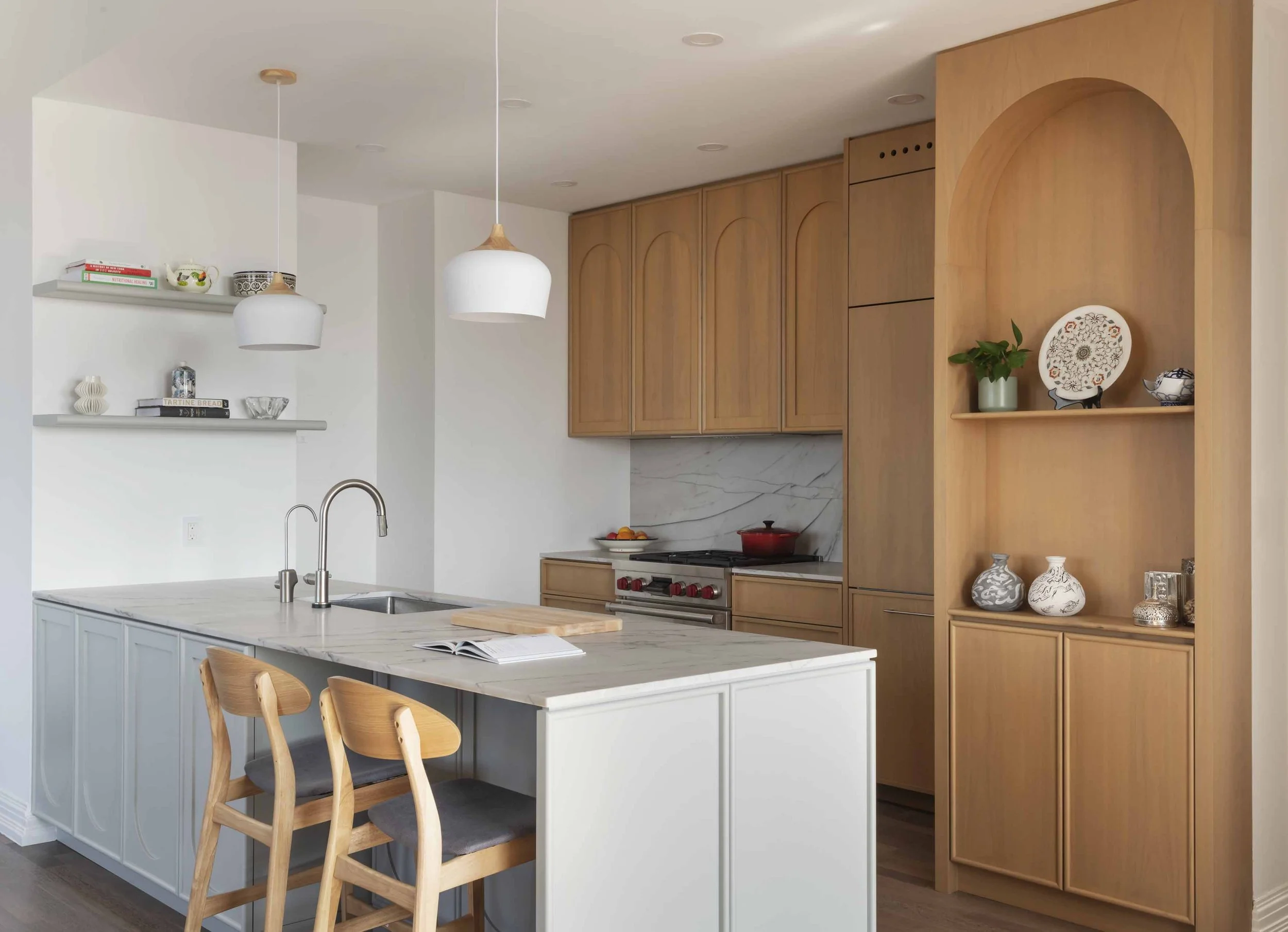 Modern kitchen with white island, wooden cabinets, open shelving, pendant lights, and decorative pottery.