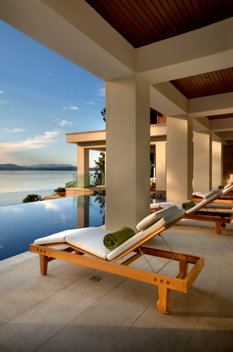 Luxury outdoor patio with lounge chairs and view of a body of water at sunset. Victoria British Columbia Custom Home. Architecture and Interior Design.