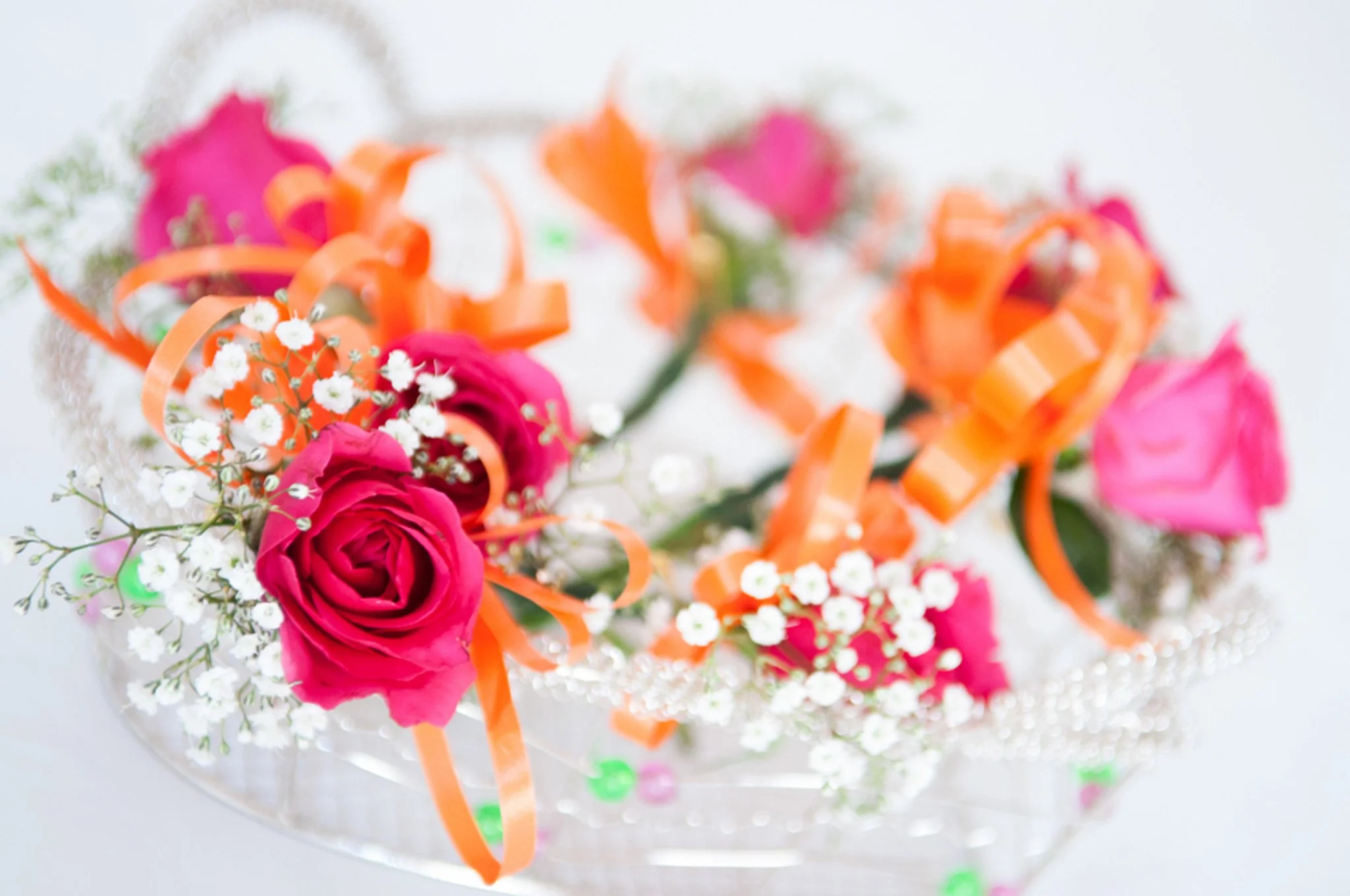 A bouquet of pink roses, white baby's breath, and orange ribbons on a white surface.