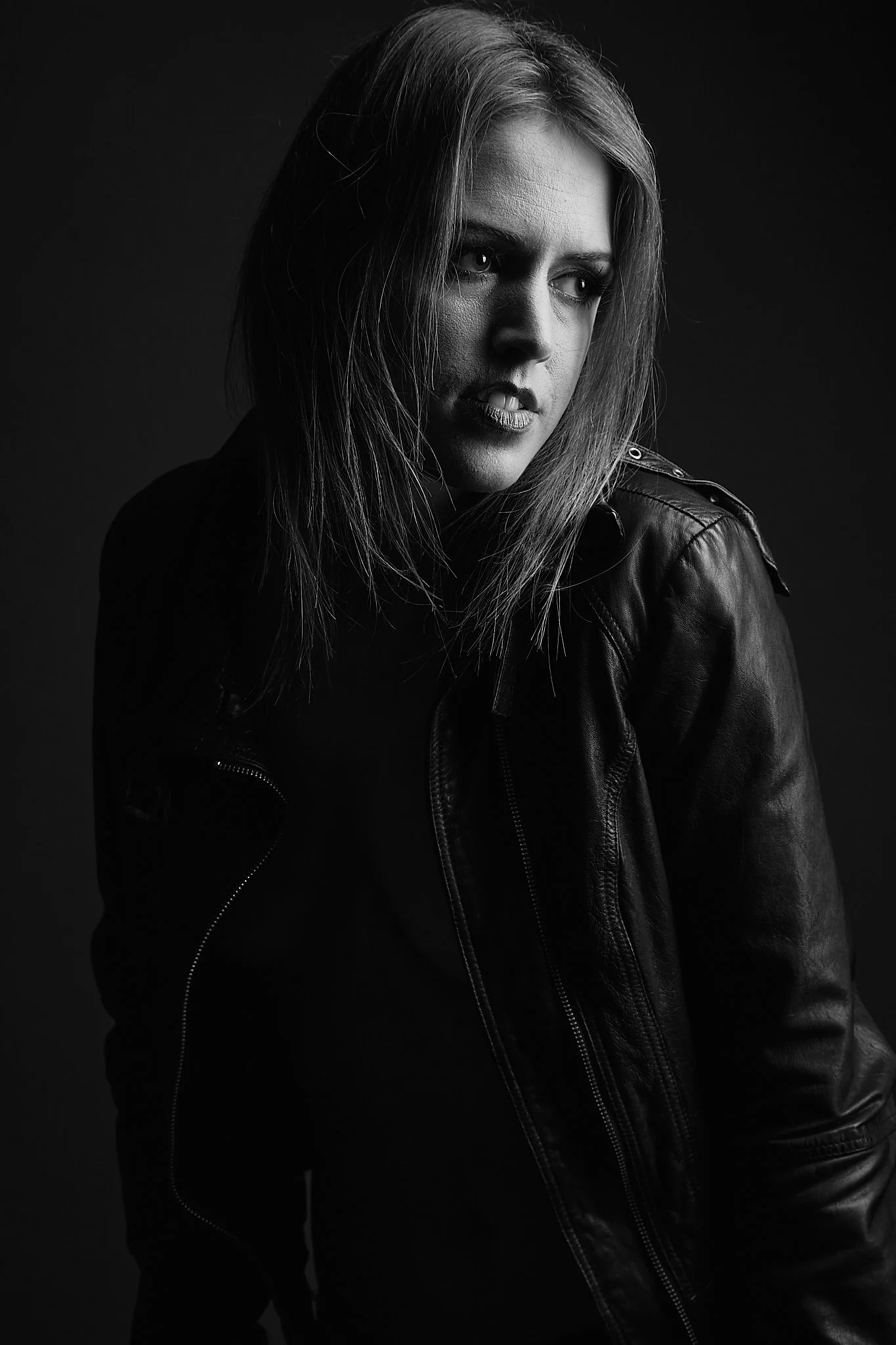Black and white portrait of a young woman with shoulder-length hair wearing a leather jacket, looking to her left with a serious expression.