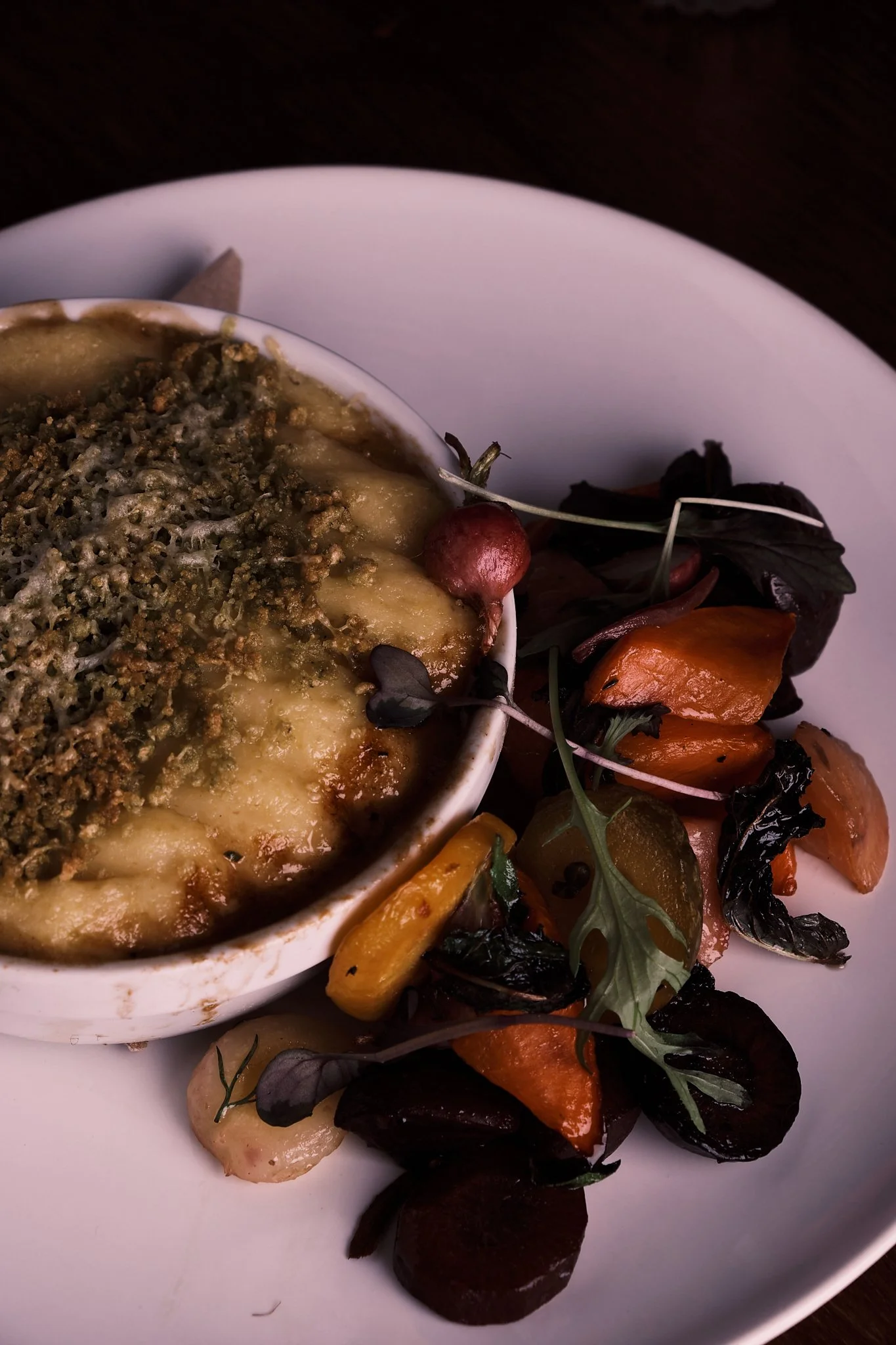 Baked dish topped with breadcrumbs served in a white ramekin, accompanied by a side of mixed roasted vegetables on a white plate.