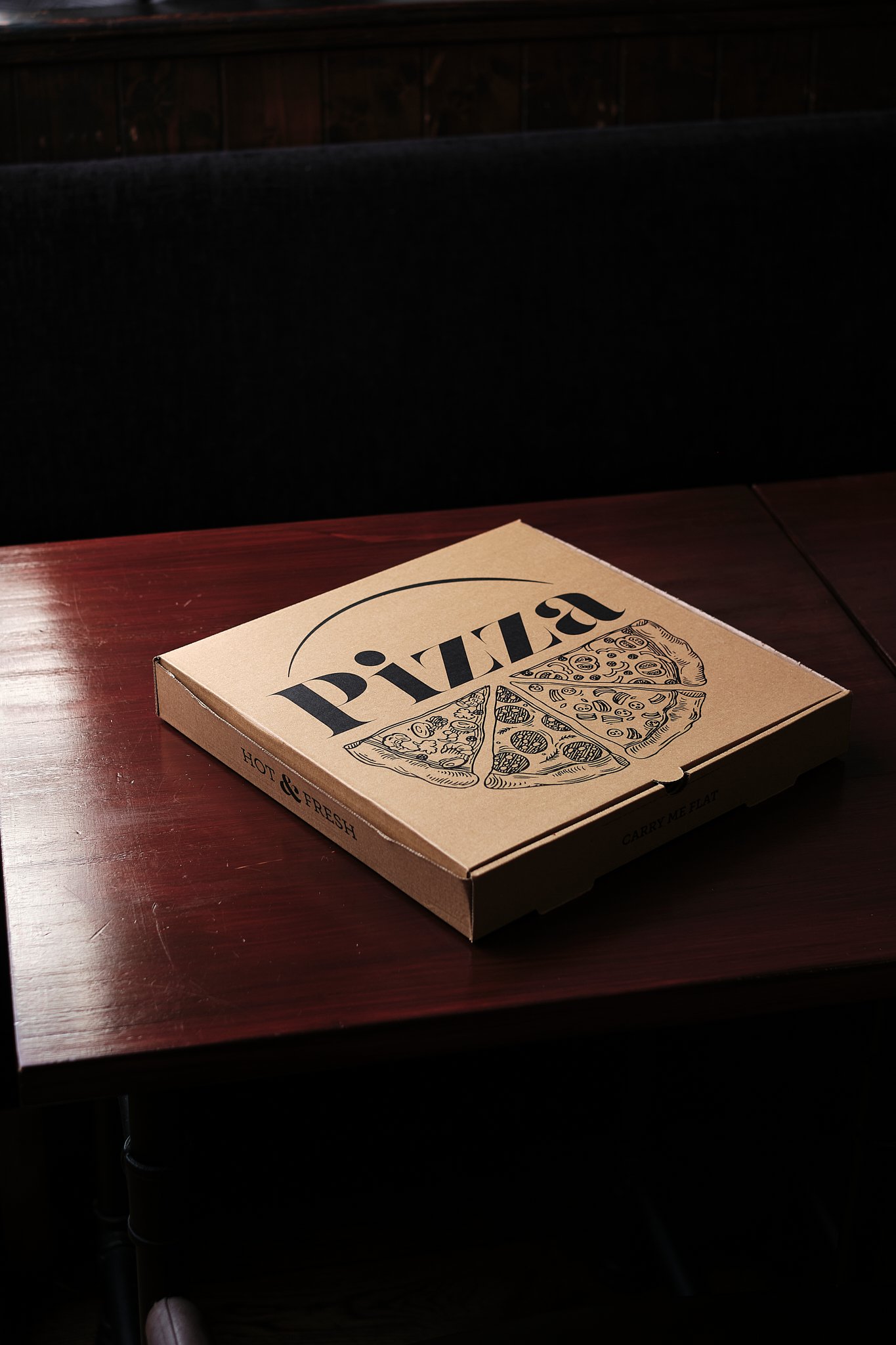 A closed pizza box on a wooden table with a dark background.