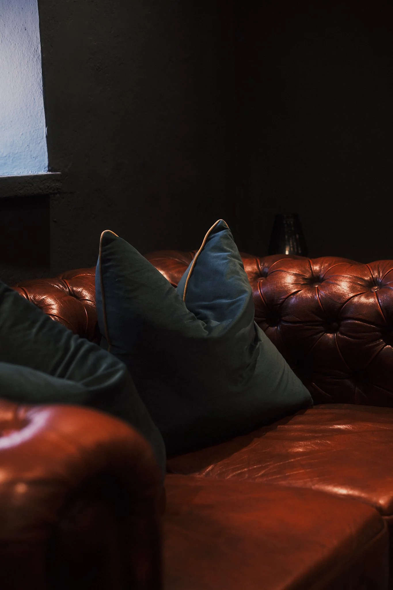 Brown leather sofa with two dark-colored pillows in a dimly lit room.