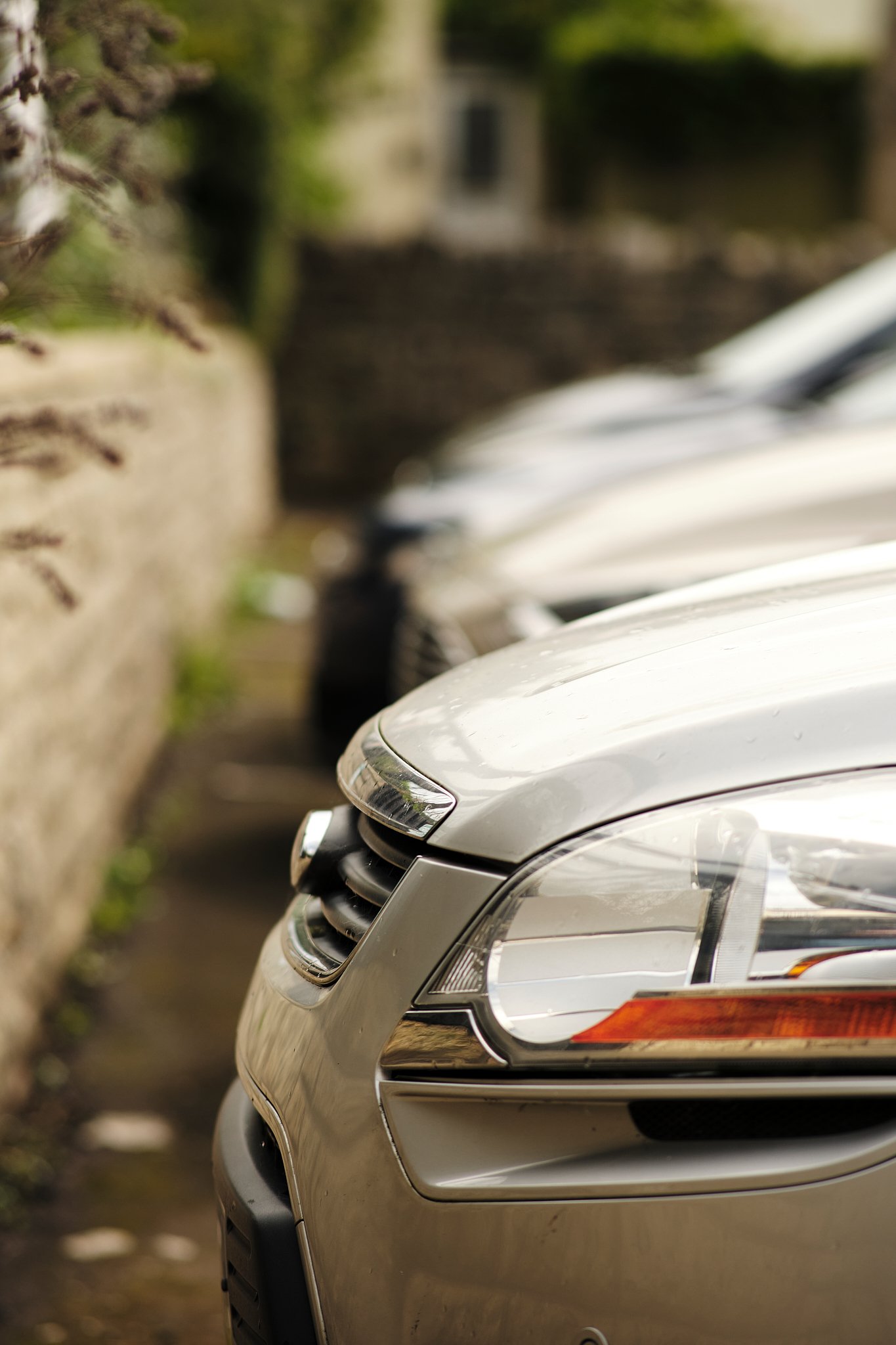 Close-up of the front part of a silver car parked along a stone wall.