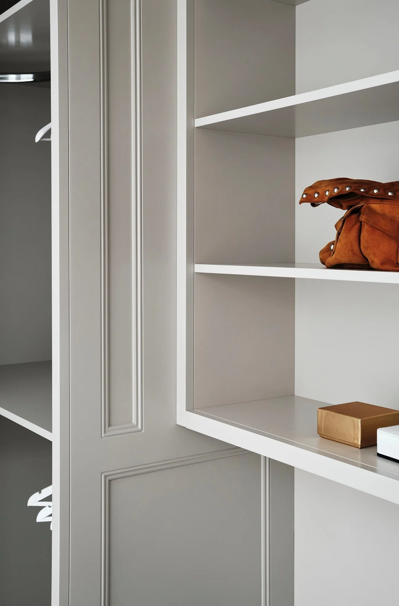 Empty white closet with beige decorative panel on the door and a few boxes and a brown purse on the shelves.