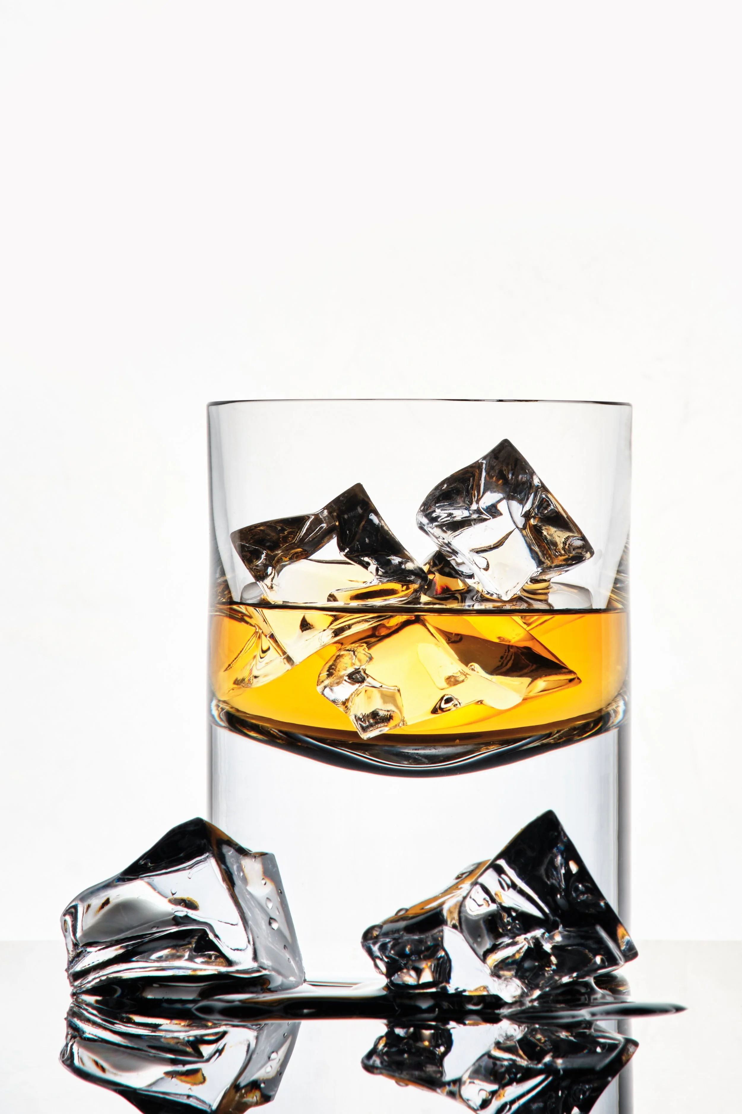 A glass of whiskey with ice cubes, with some ice cubes on the surface and inside the glass, against a white background.