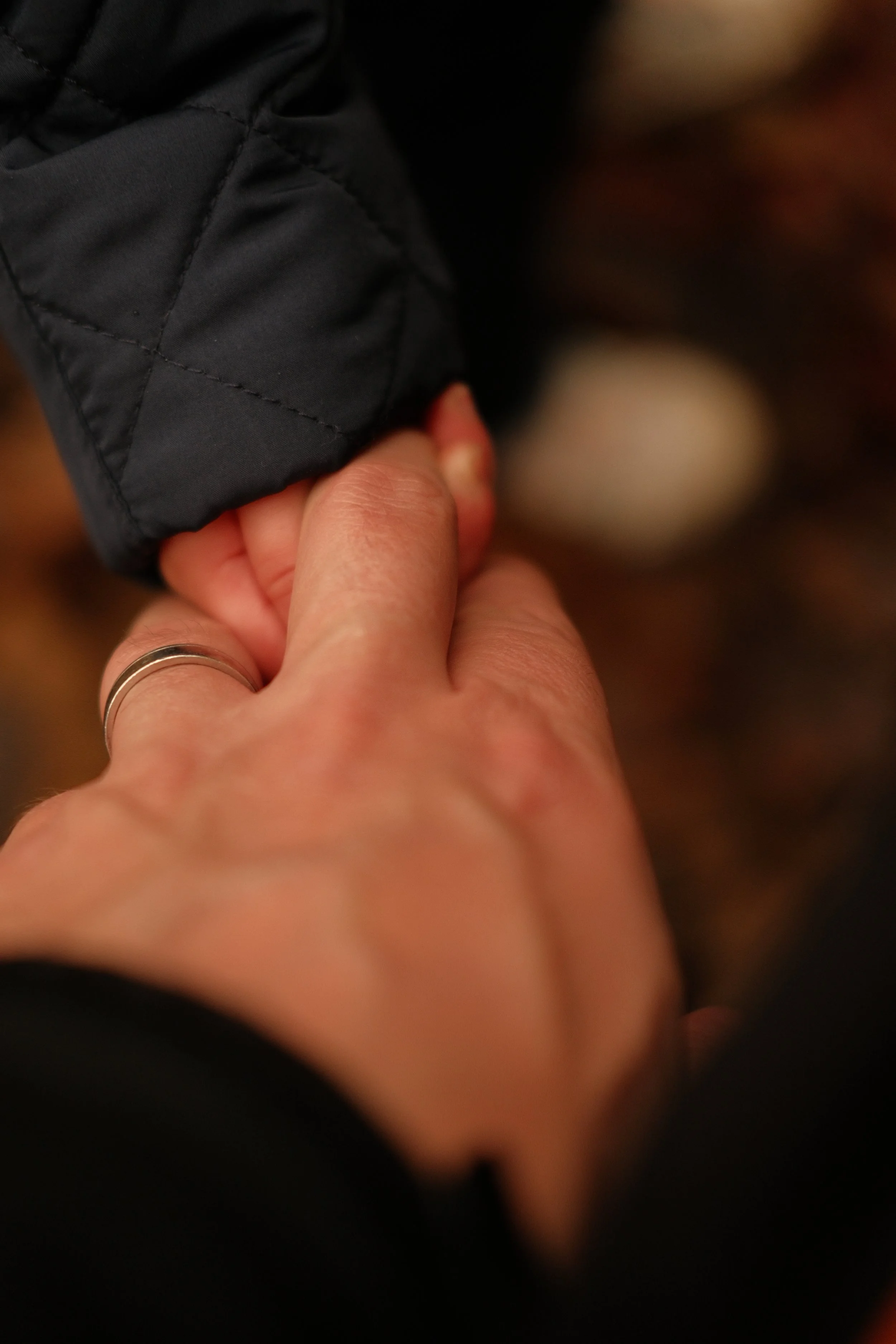 Close-up of an adult holding a child's hand, with the child wearing a black quilted sleeve.