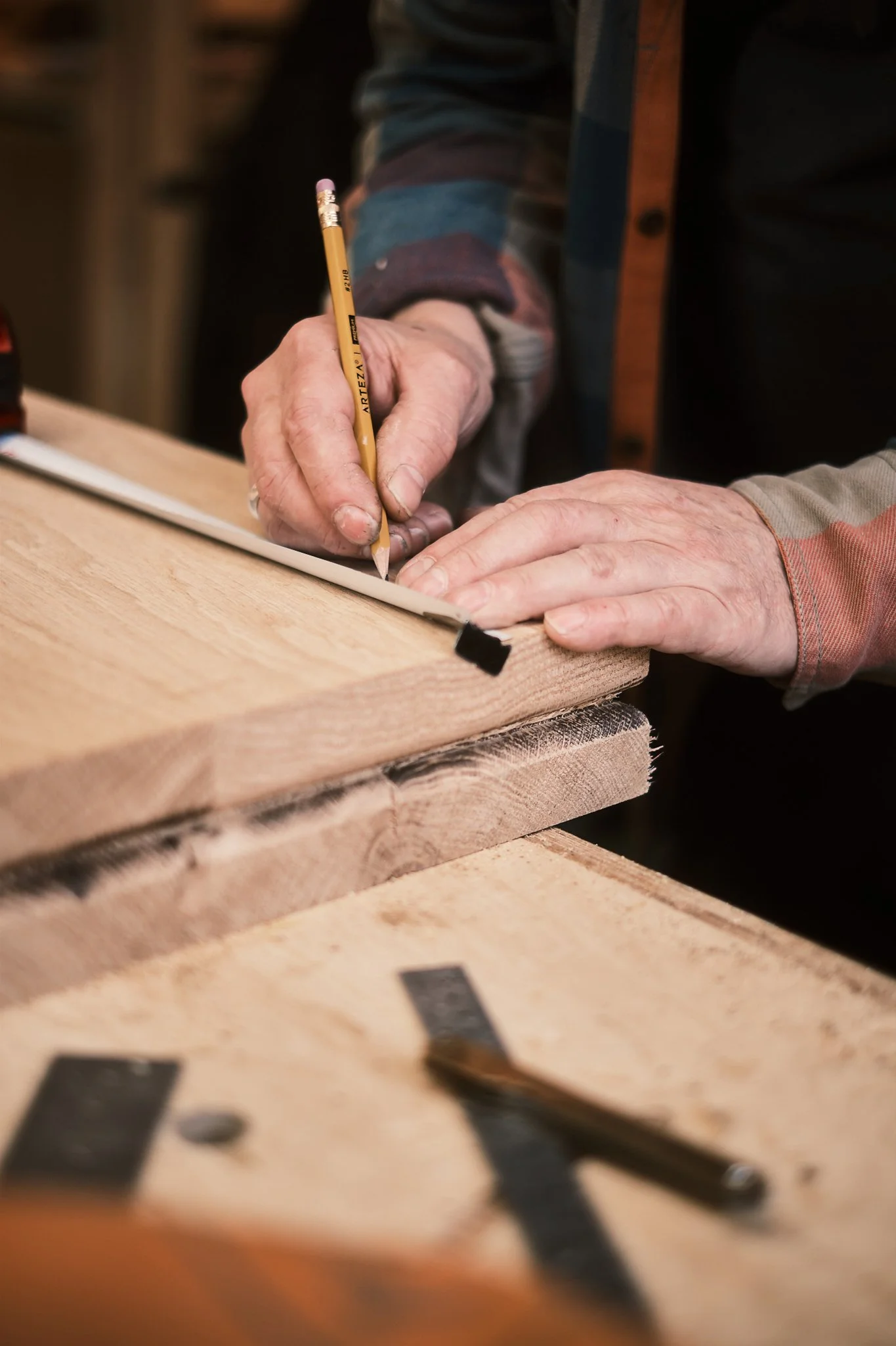A person marks a piece of wood with a pencil for cutting or shaping in a woodworking shop.