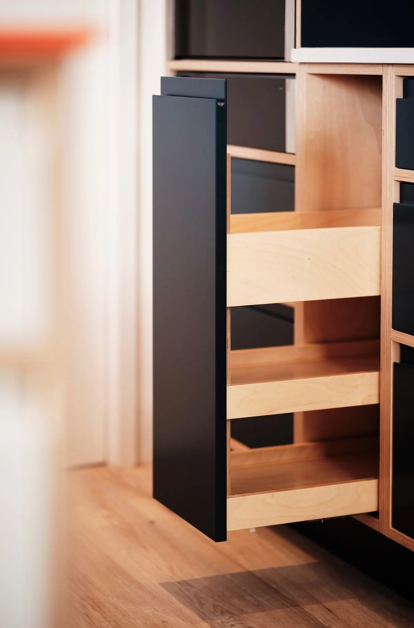 Open cabinet with wooden shelves and black sides in a room with wooden flooring.