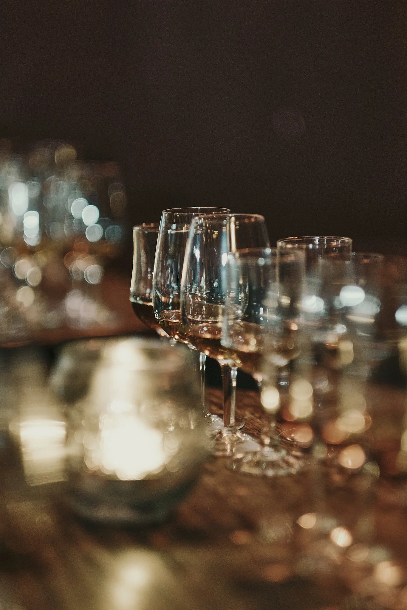 A row of wine glasses filled with red wine on a table, with a blurred background of additional glasses and a cozy, dimly lit atmosphere.