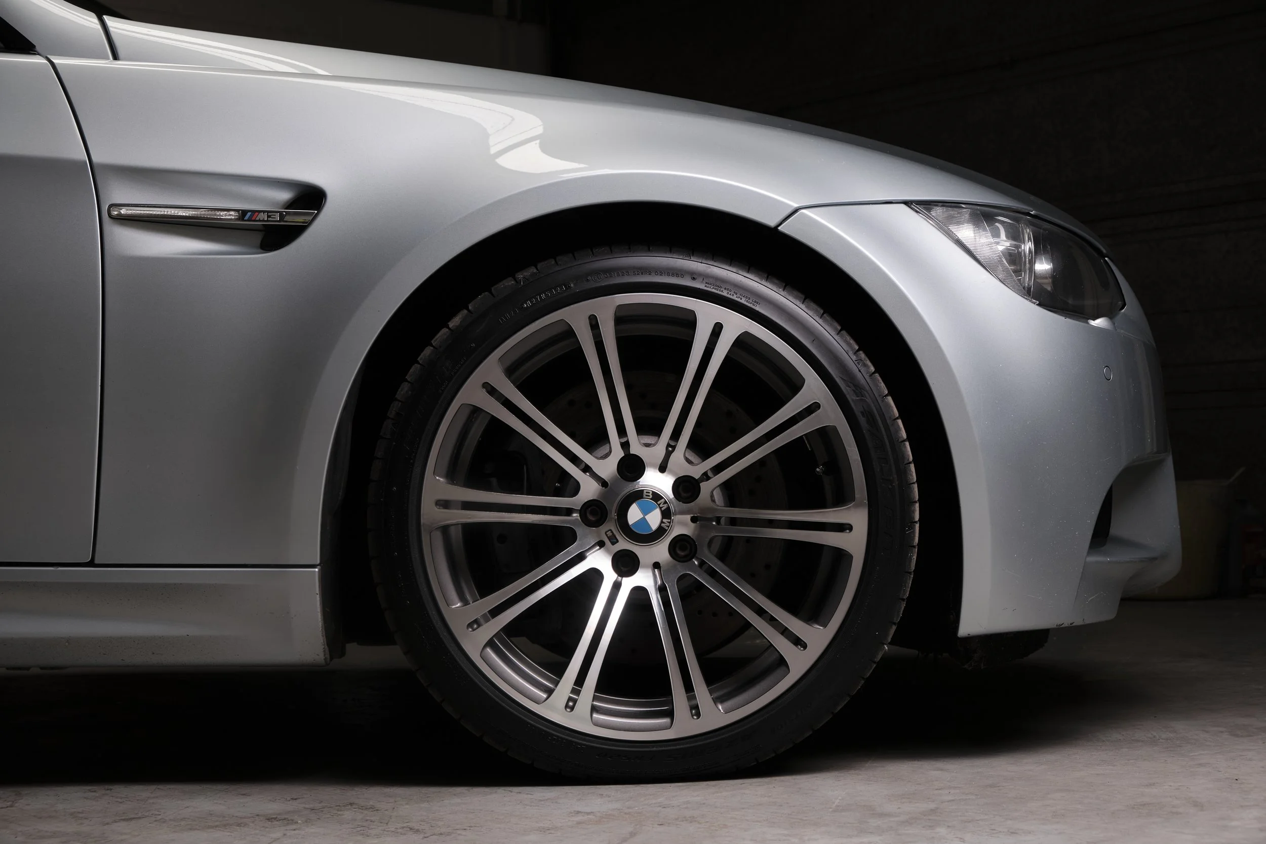 Close-up of a silver BMW car's front wheel and fender in a dimly lit garage