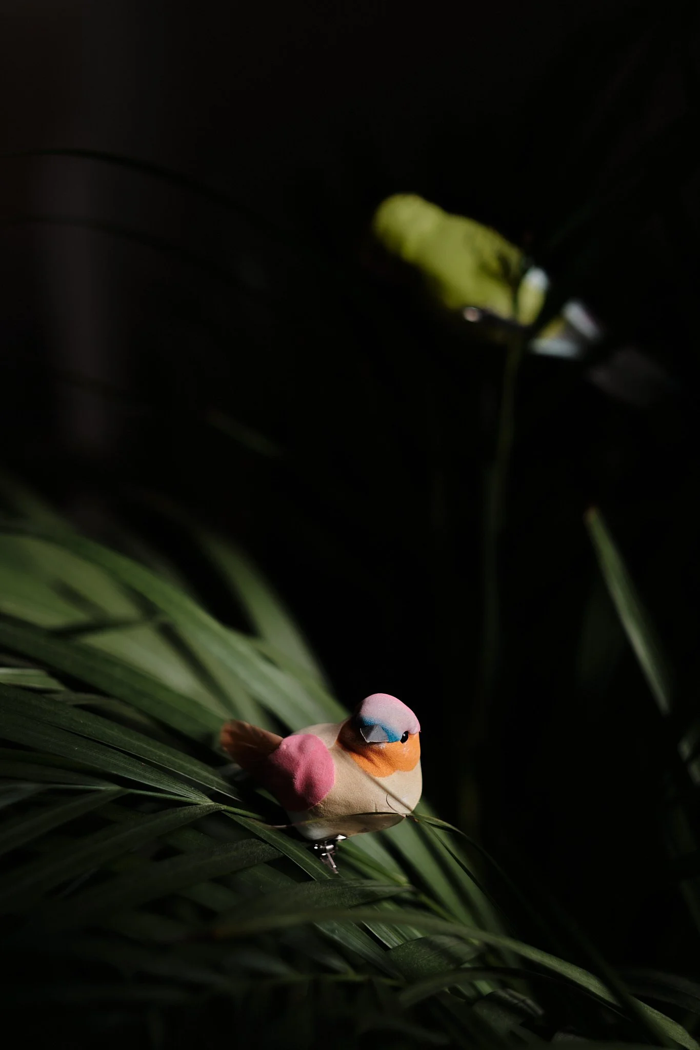 Colorful sparrow figurine resting on green leaves with dark background