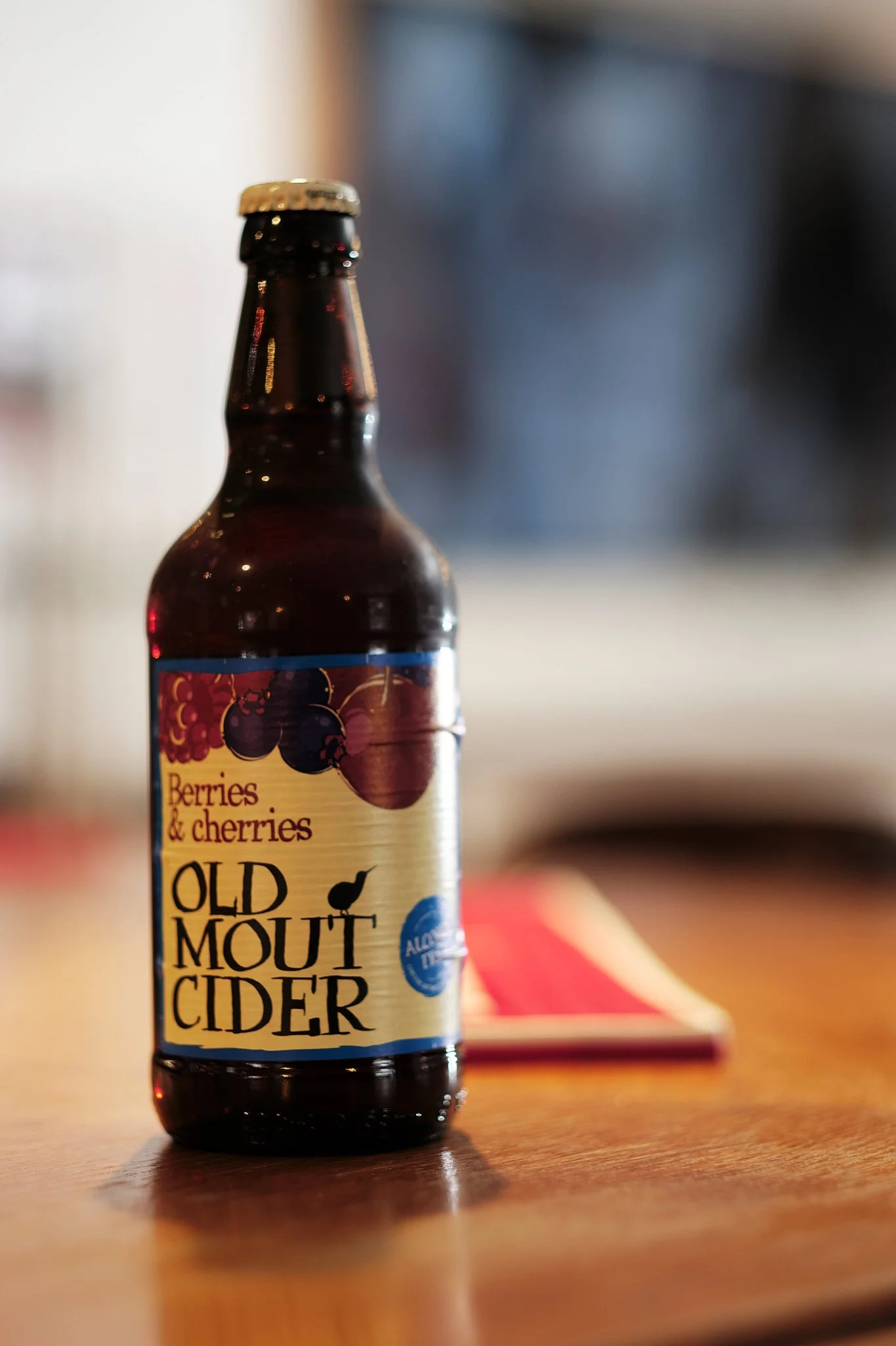 A bottle of Old Mout Cider with a label featuring berries and cherries on a wooden table.