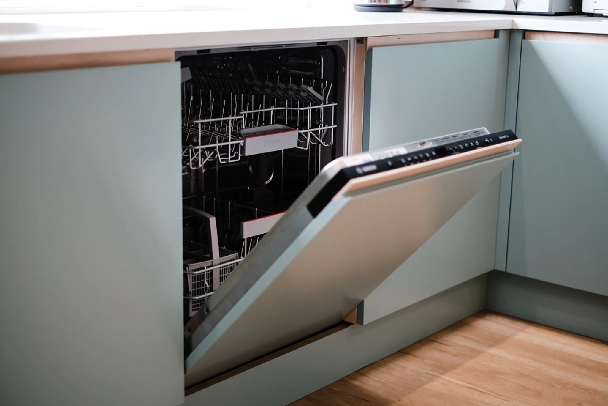 Open dishwasher with empty racks in a kitchen cabinet.